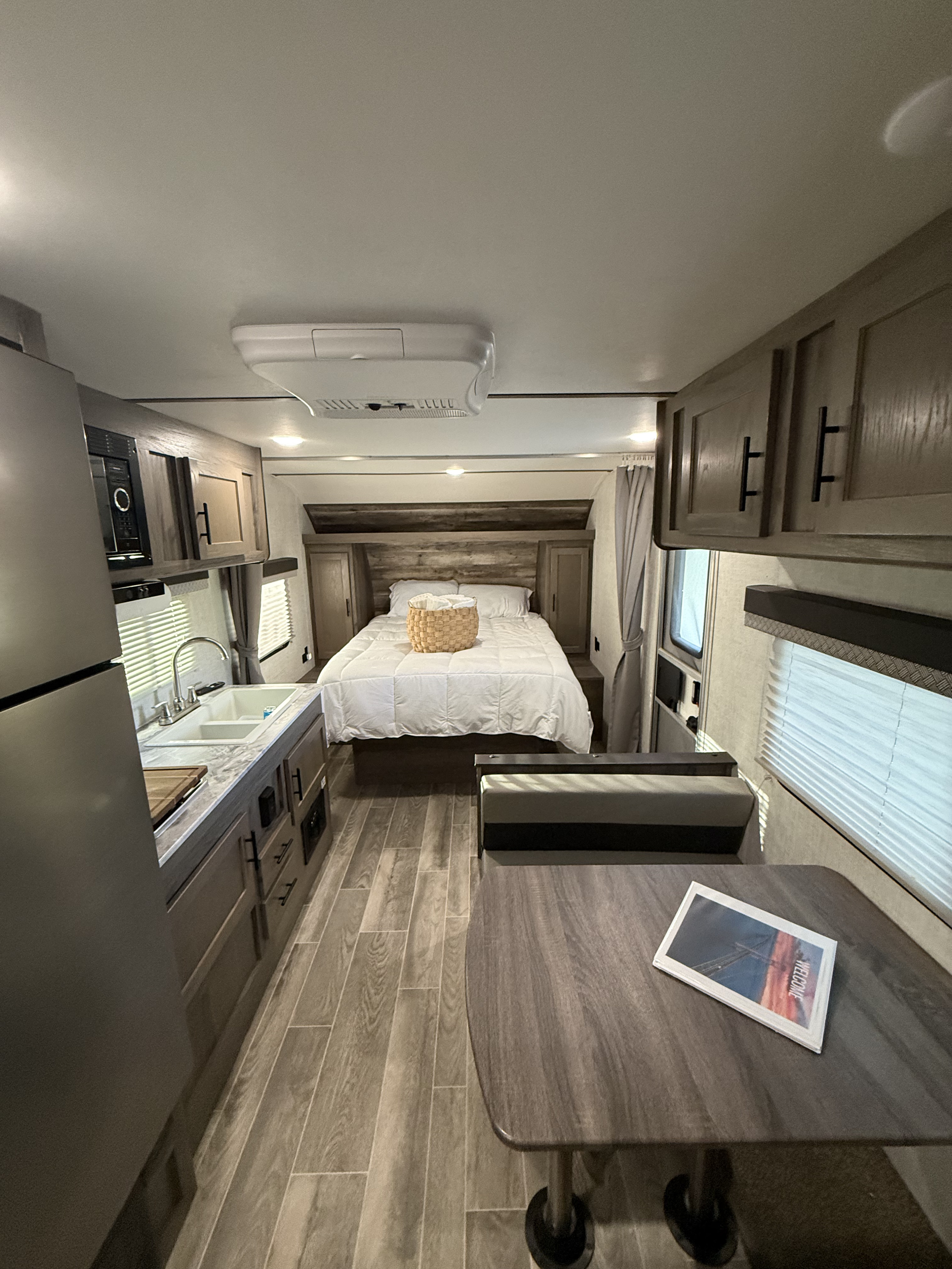 Bright RV rental interior: cozy bed, compact kitchen with sink, and a dinette area with seating and table.. Gulf Stream Ameri-Lite 2021
