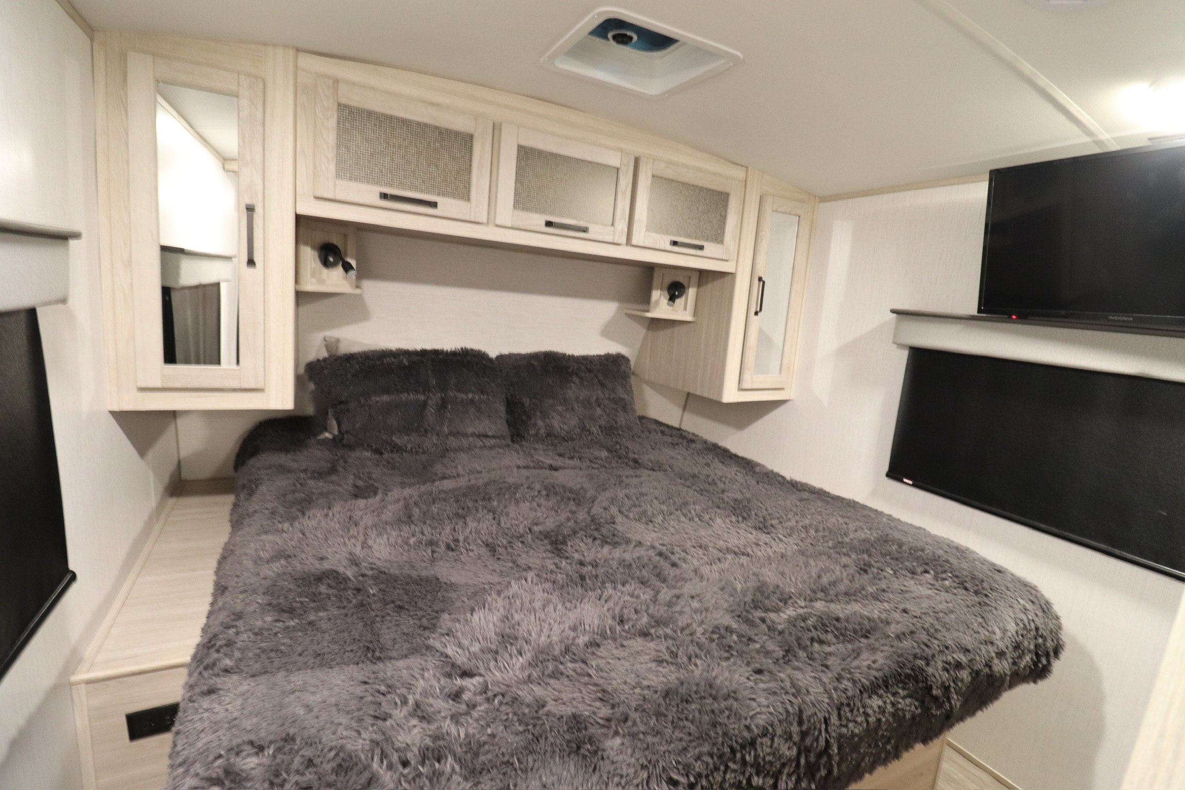 Cozy RV rental bedroom featuring a plush grey bed, light wood cabinets, wall-mounted TV, and side storage.. Twilight RVS Signature 2021