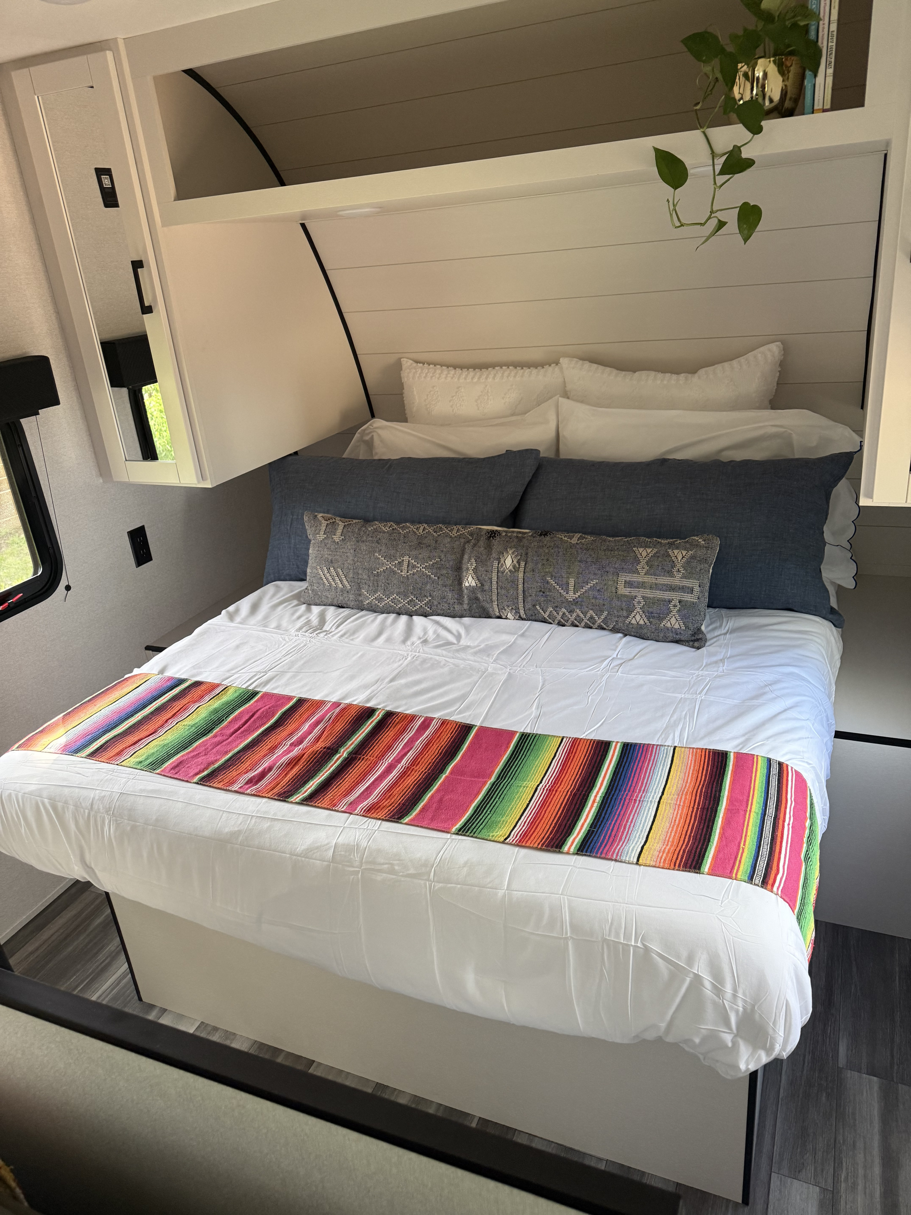 Cozy RV rental bedroom with a neatly made bed, blue pillows, colorful striped runner, white shiplap walls, and overhead storage.. Jayco Jay Flight 260BH 2026