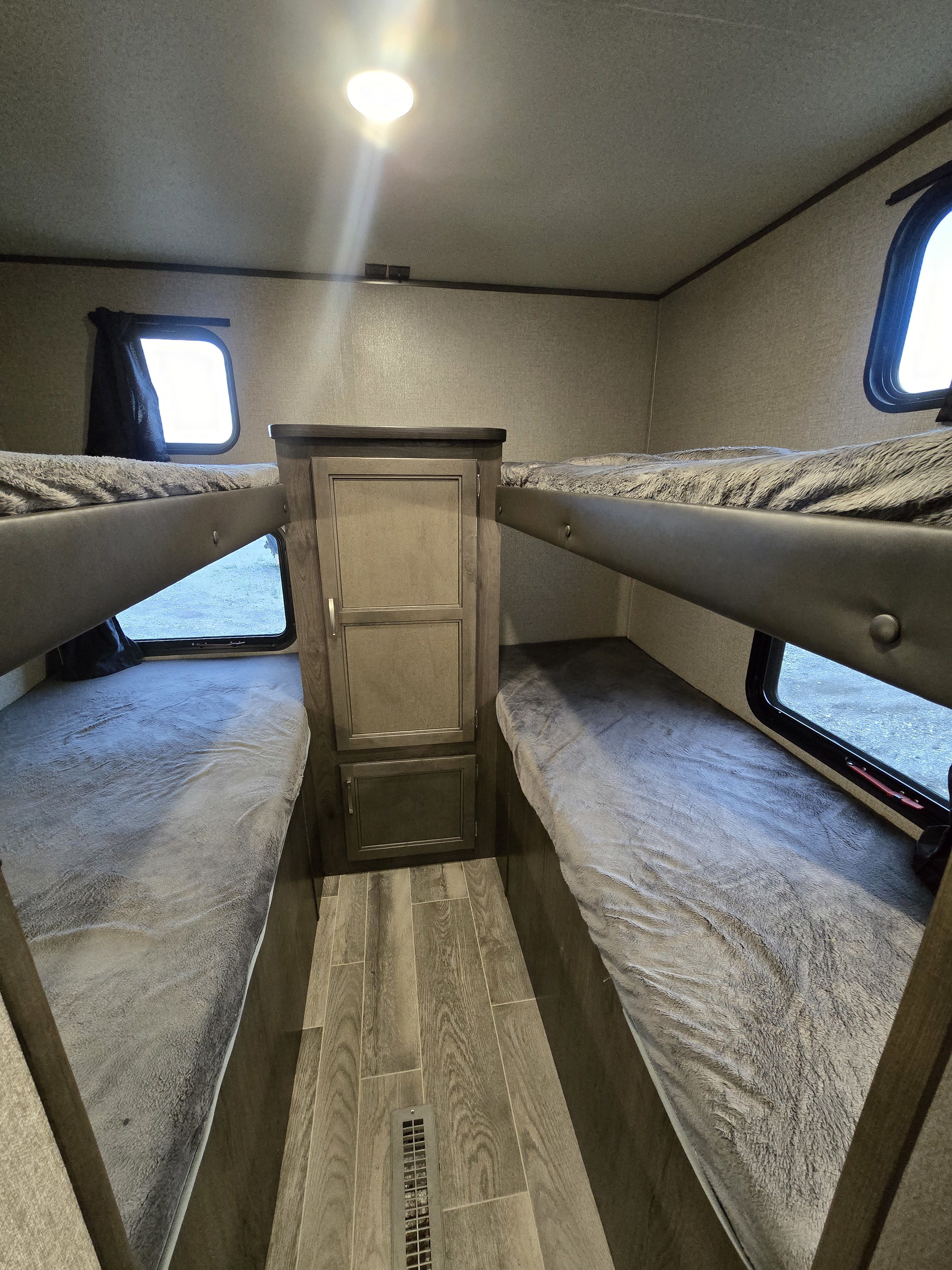 Inside an RV rental: a comfortable bunk bed sleeping area with two beds, soft blankets, central storage, and windows.. jayco Jay Flight 2020