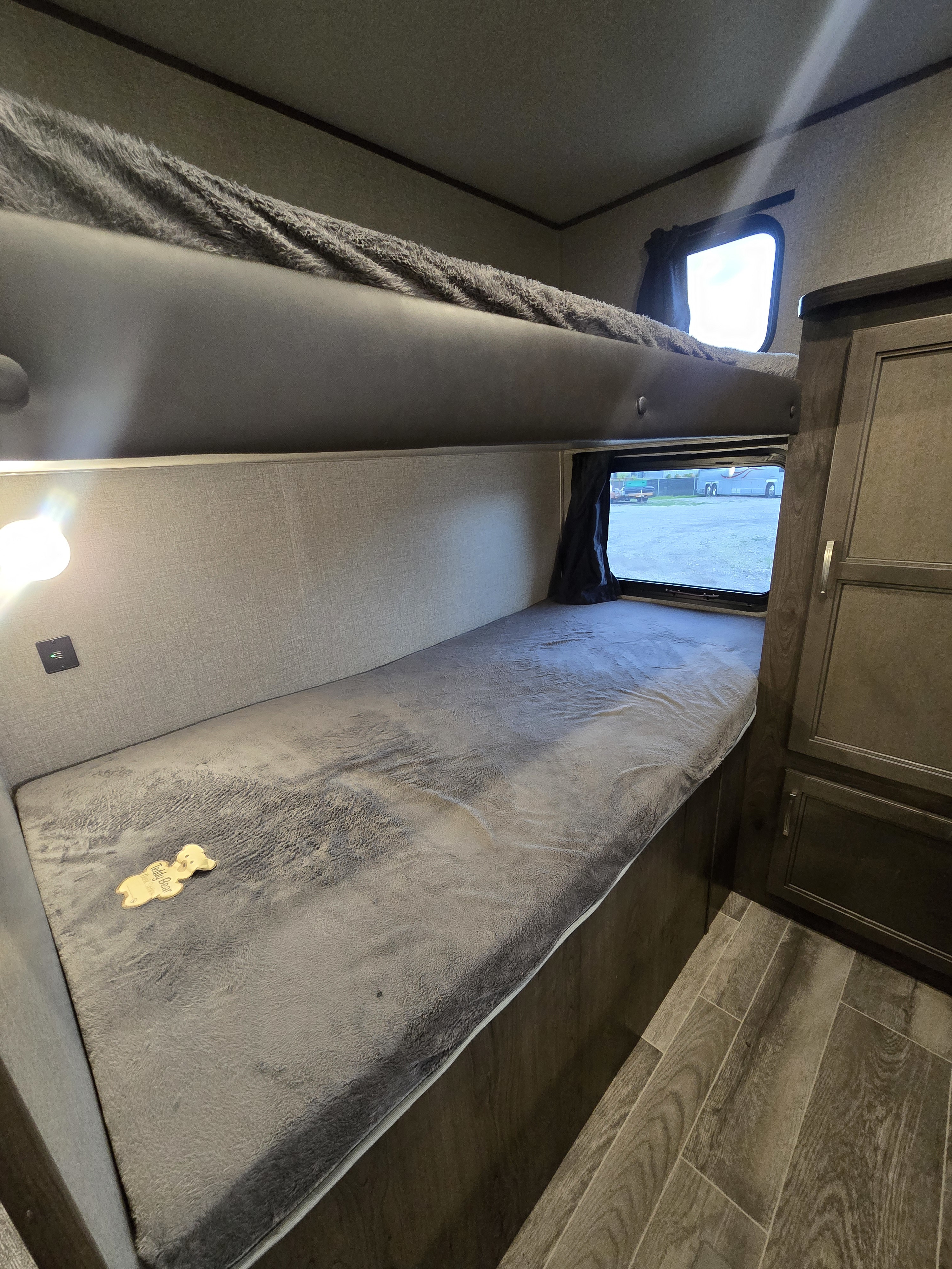 RV rental bunk bedroom: comfy gray bedding, a window overlooking the outdoors, and a practical charging port, ready for adventure.. jayco Jay Flight 2020