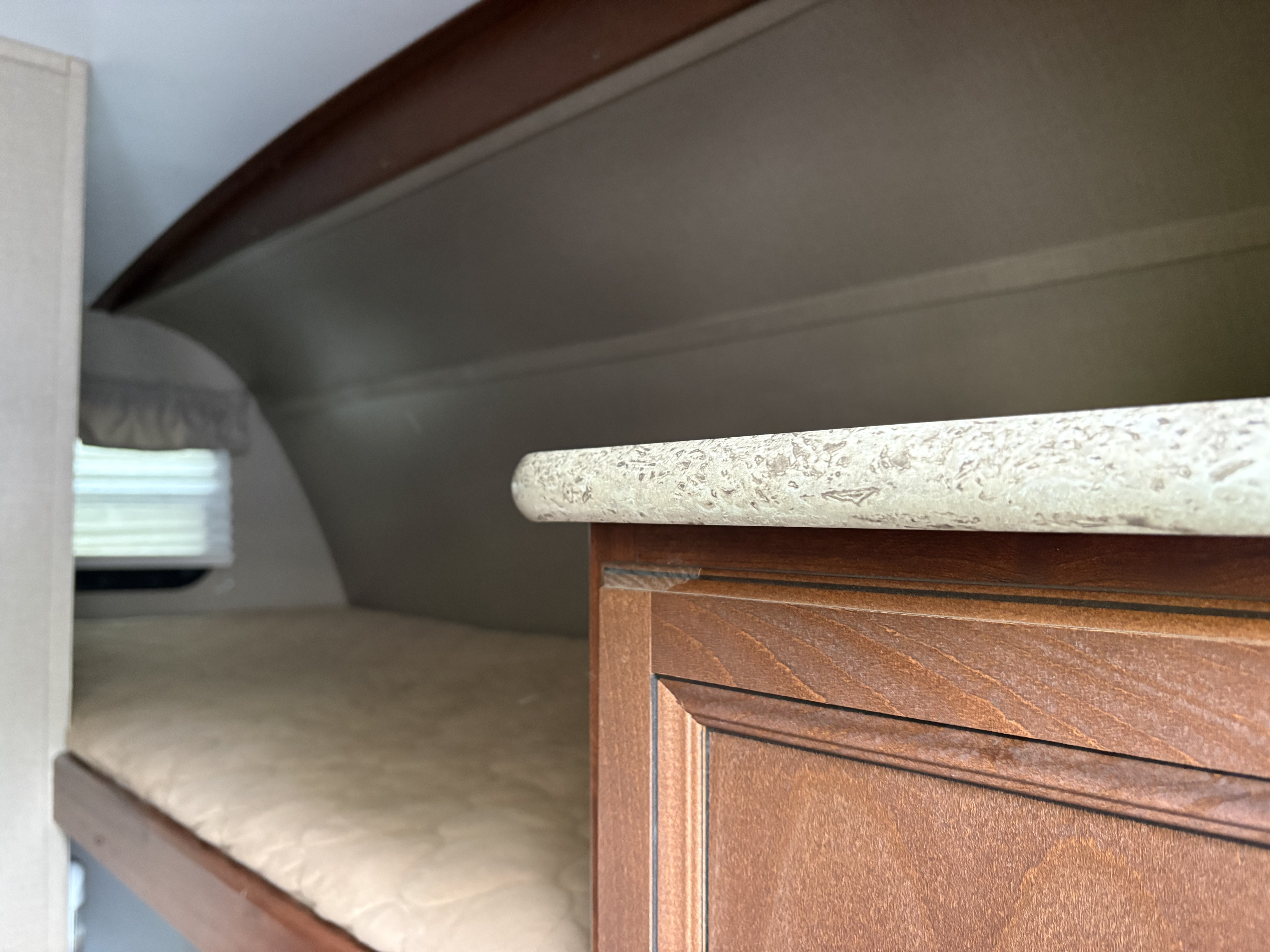 An RV rental interior with a bunk bed, a window, and a cabinet with a speckled countertop in the foreground.. Keystone RV Outback Terrain 2016