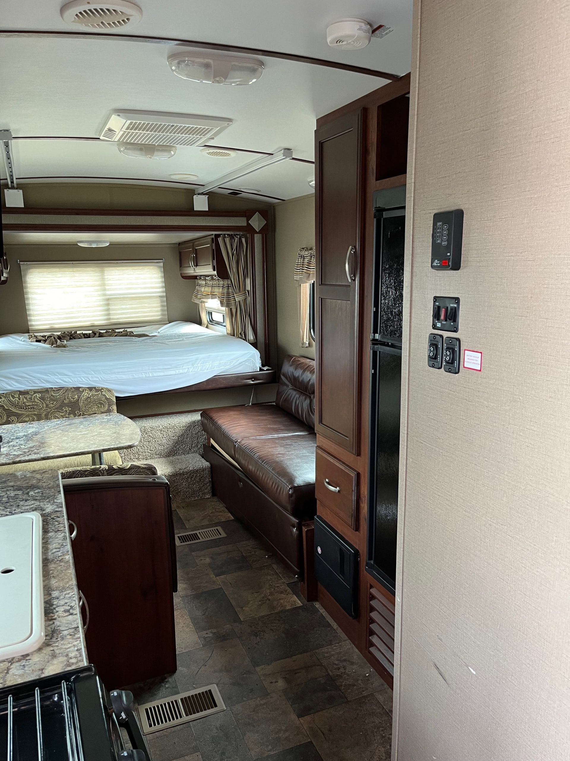 Spacious RV rental interior featuring a cozy bed, brown leather sofa, dinette, and functional kitchen area.. Keystone RV Outback Terrain 2016