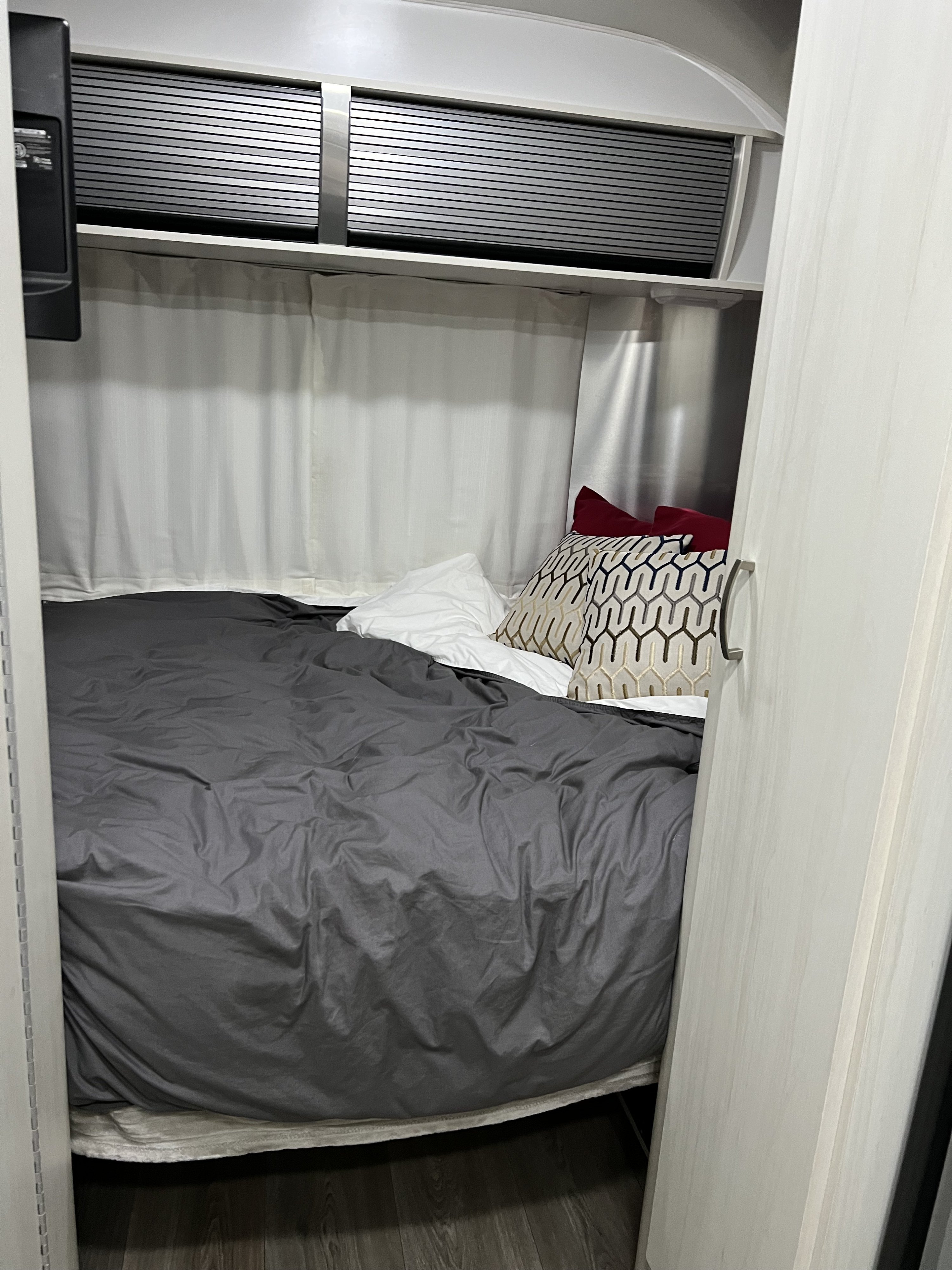 Inside an RV rental: a compact bedroom featuring a bed with grey duvet, patterned pillows, and sleek overhead cabinets.. Airstream Sport 2016