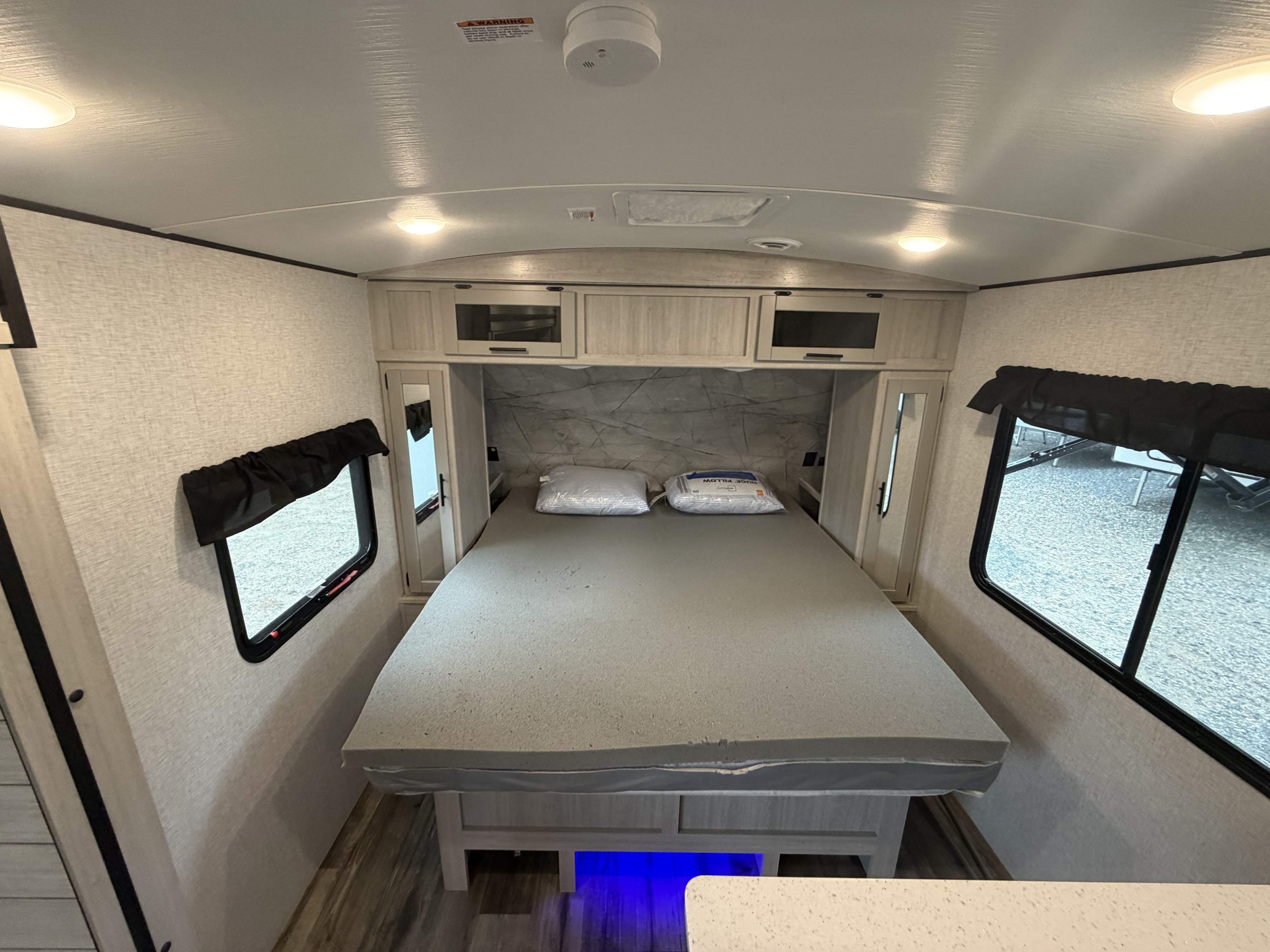Interior of a clean rv rental bedroom with a comfy gray bed, mirrored closet, overhead storage, and windows for natural light.. Crossroads RV Sunset Trail Super Lite 2024