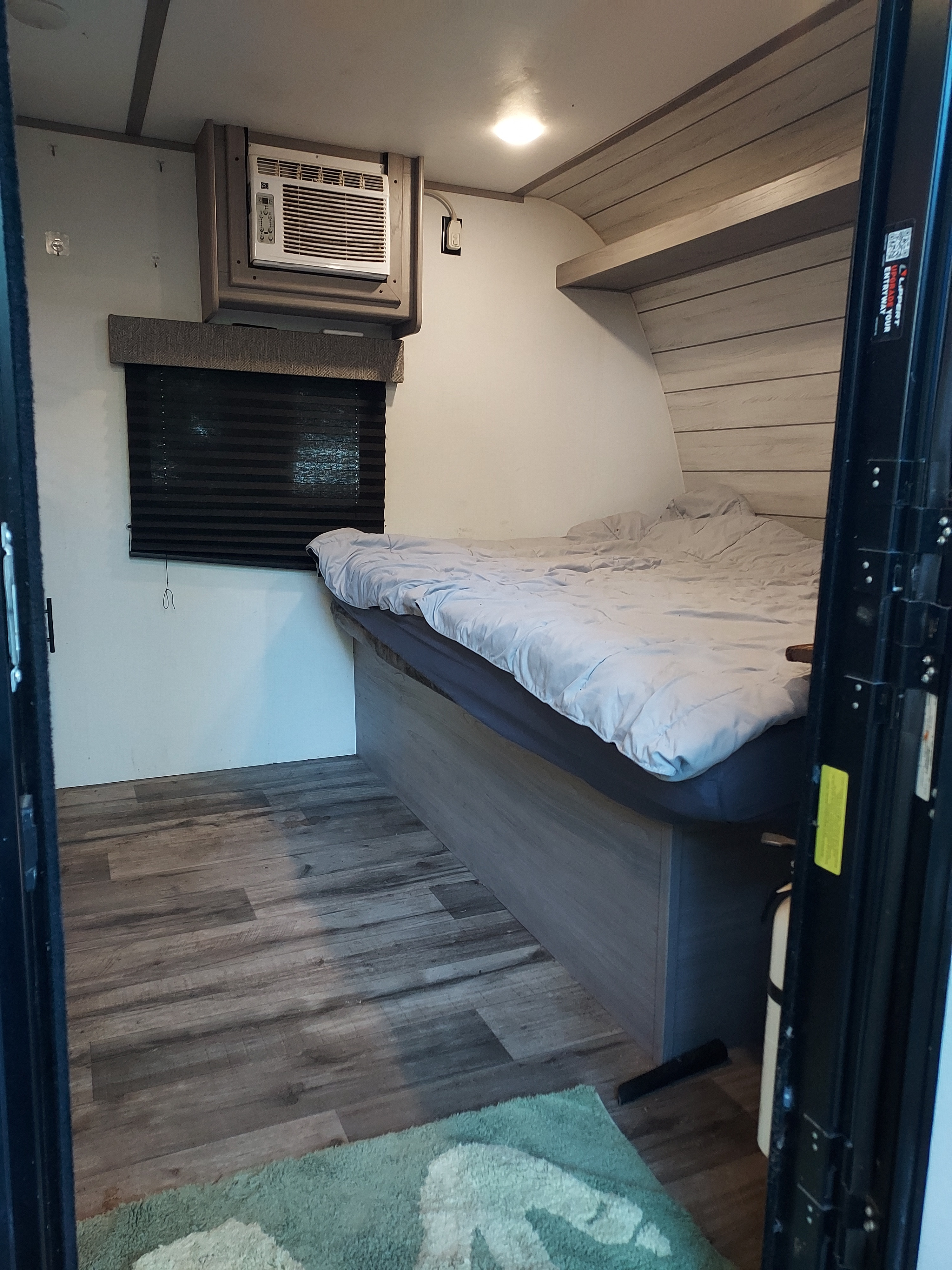 Cozy RV rental bedroom featuring a bed, window AC, wood-look floor, and a visible fire extinguisher for safety.. Dutchmen Coleman Lantern LT 2024