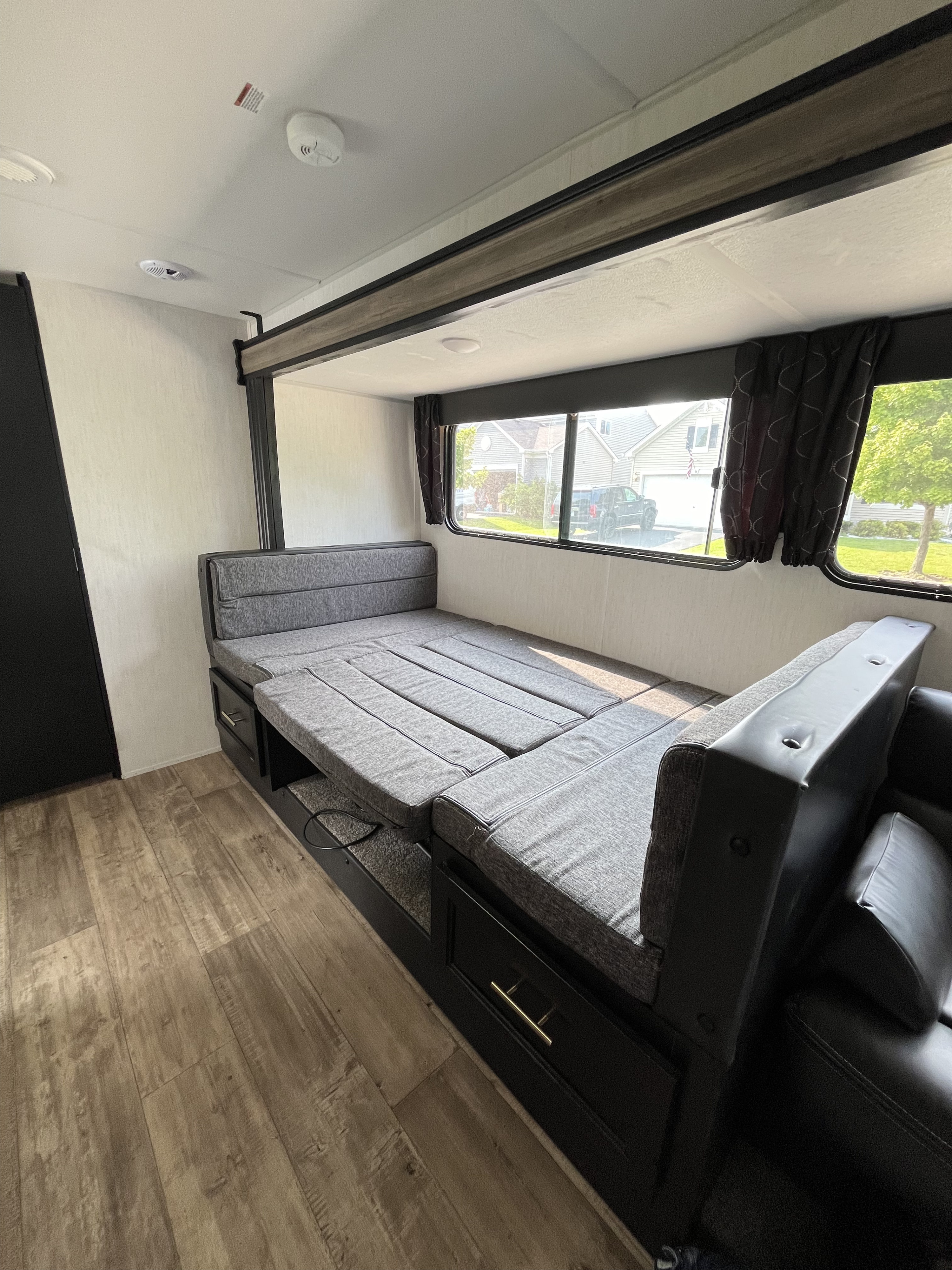 RV rental interior: Flexible gray bunk/dinette seating converts to a bed, featuring wood-look floors, storage, and large windows.. Forest River Cherokee Grey Wolf 2022