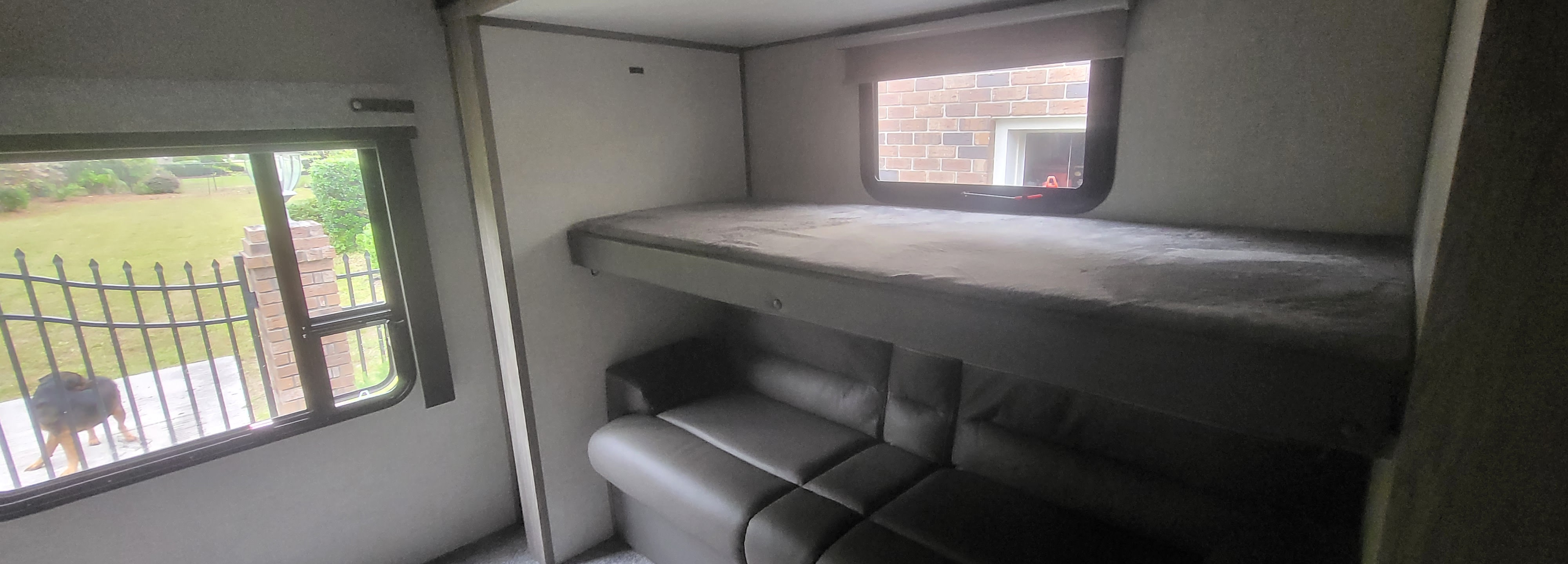 Cozy RV rental featuring bunk beds and a sofa. Windows offer views of a yard with a dog and a brick building.. Forest River Salem Hemisphere 2021
