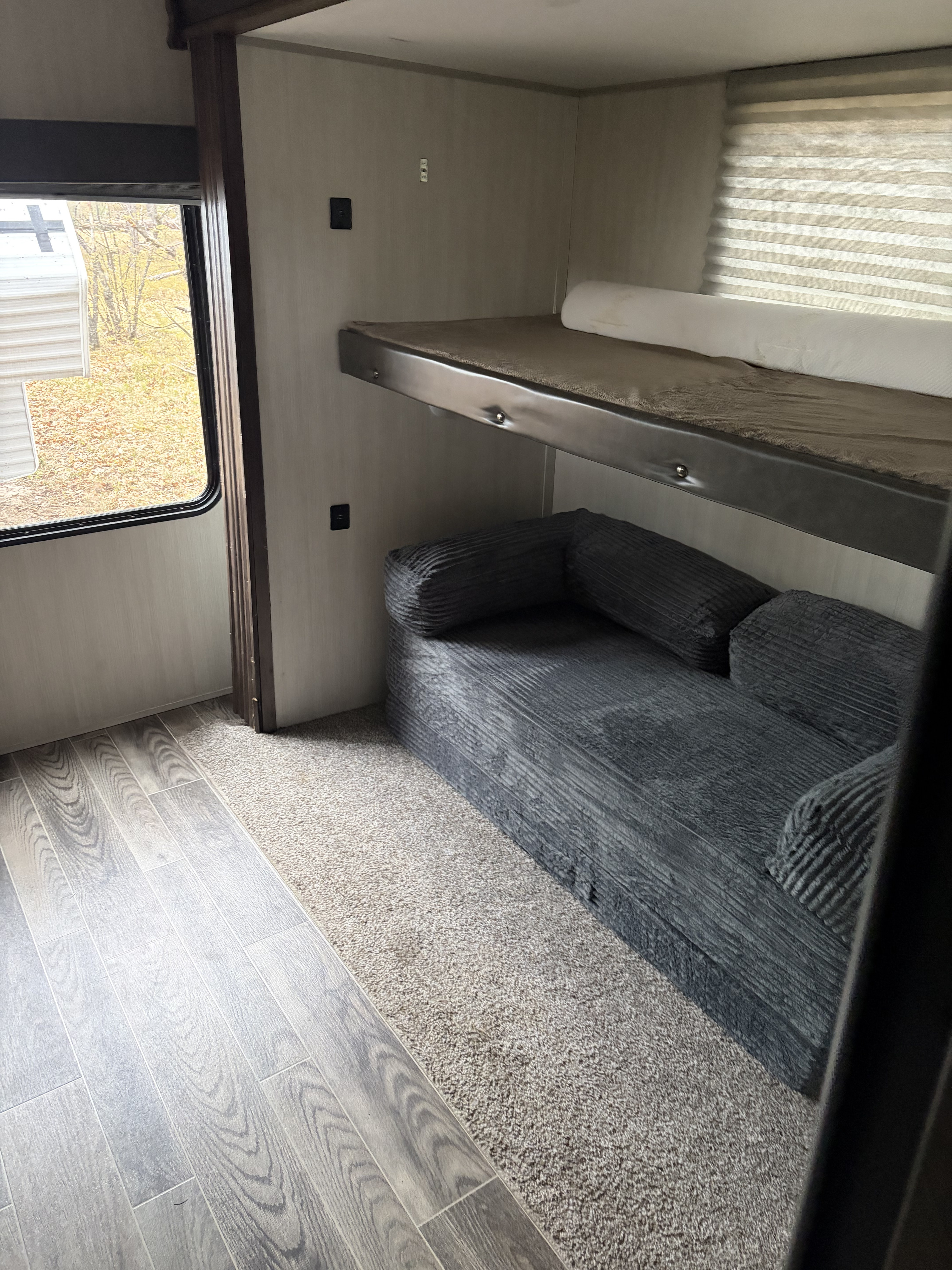 Cozy RV rental interior showcasing bunk beds over a sofa, wood-look flooring, and a large window with blinds.. Forest River Cherokee 2019