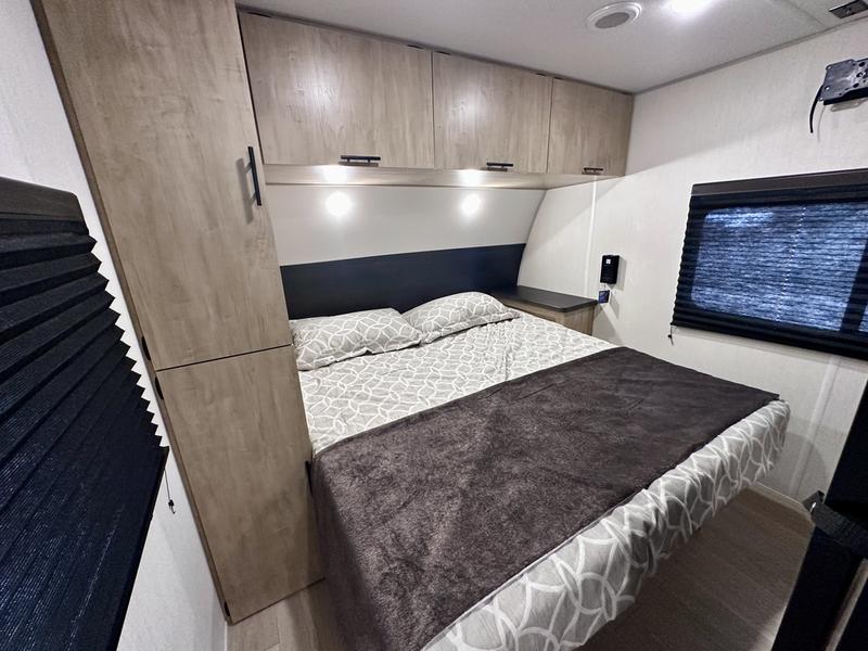 Modern RV rental bedroom with a comfy bed, wood cabinets, and window blinds, ideal for a cozy getaway on wheels.. Forest River Cherokee 26KF 2026