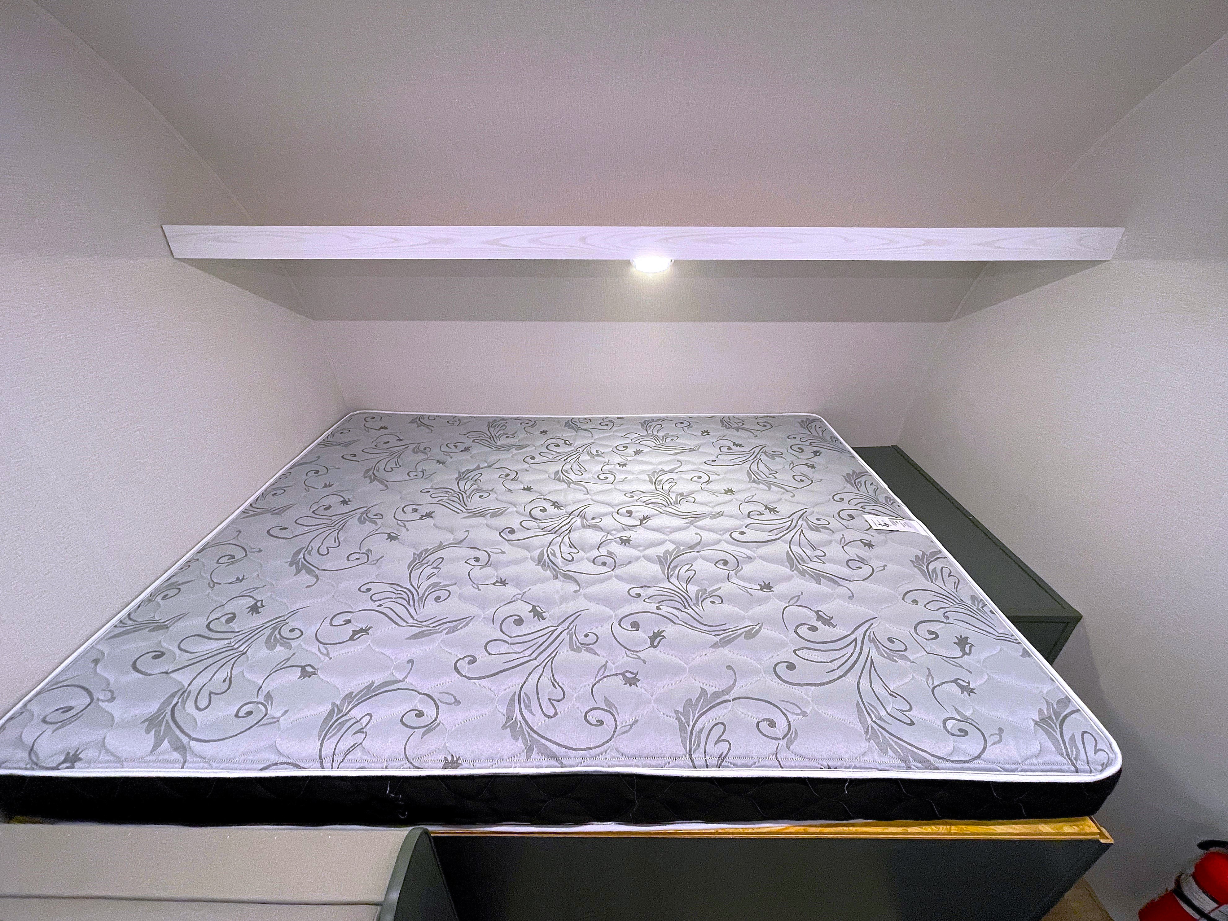 RV rental: Floral-patterned mattress in a snug sleeping alcove, illuminated by an overhead light on a shelf.. Heartland RVs Eddie Bauer 2025