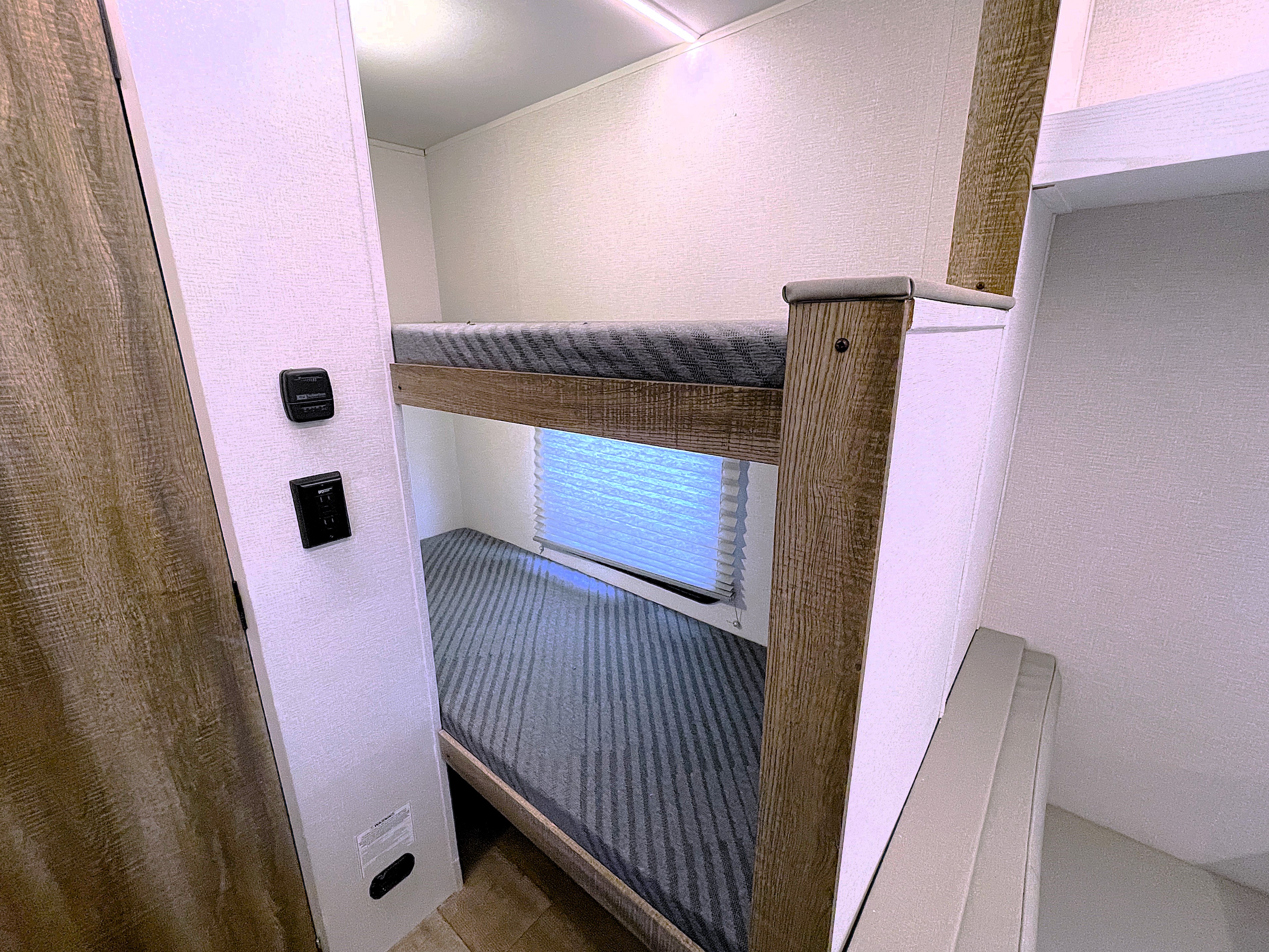 Cozy bunk beds within an RV rental, featuring controls and window blinds for comfortable compact sleeping accommodations.. Heartland RVs Eddie Bauer 2025