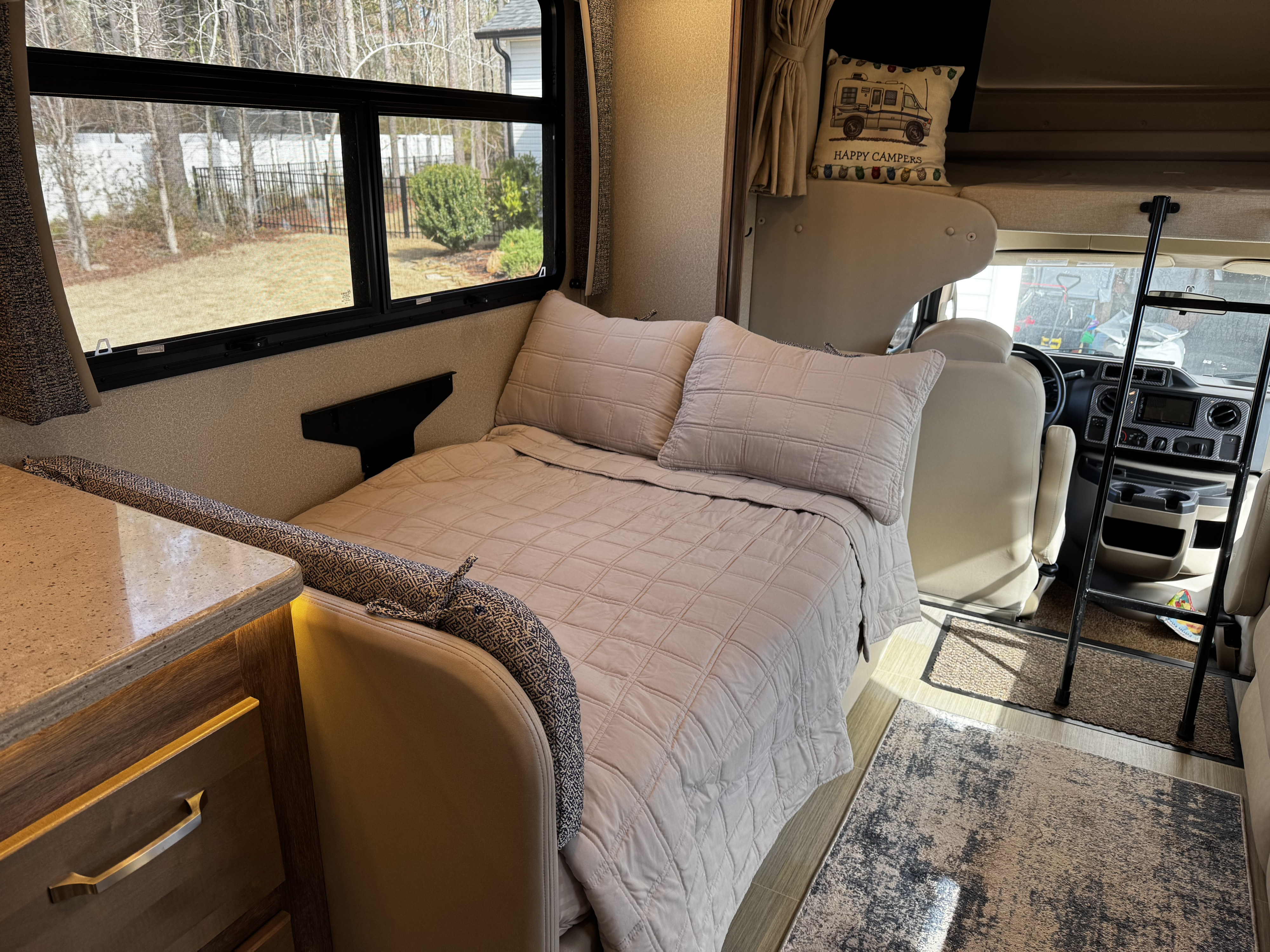 Cozy RV rental interior featuring a comfy bed, large window view, and the driver's cab area. Ideal for camping trips.. Jayco Greyhawk Prestige 2020