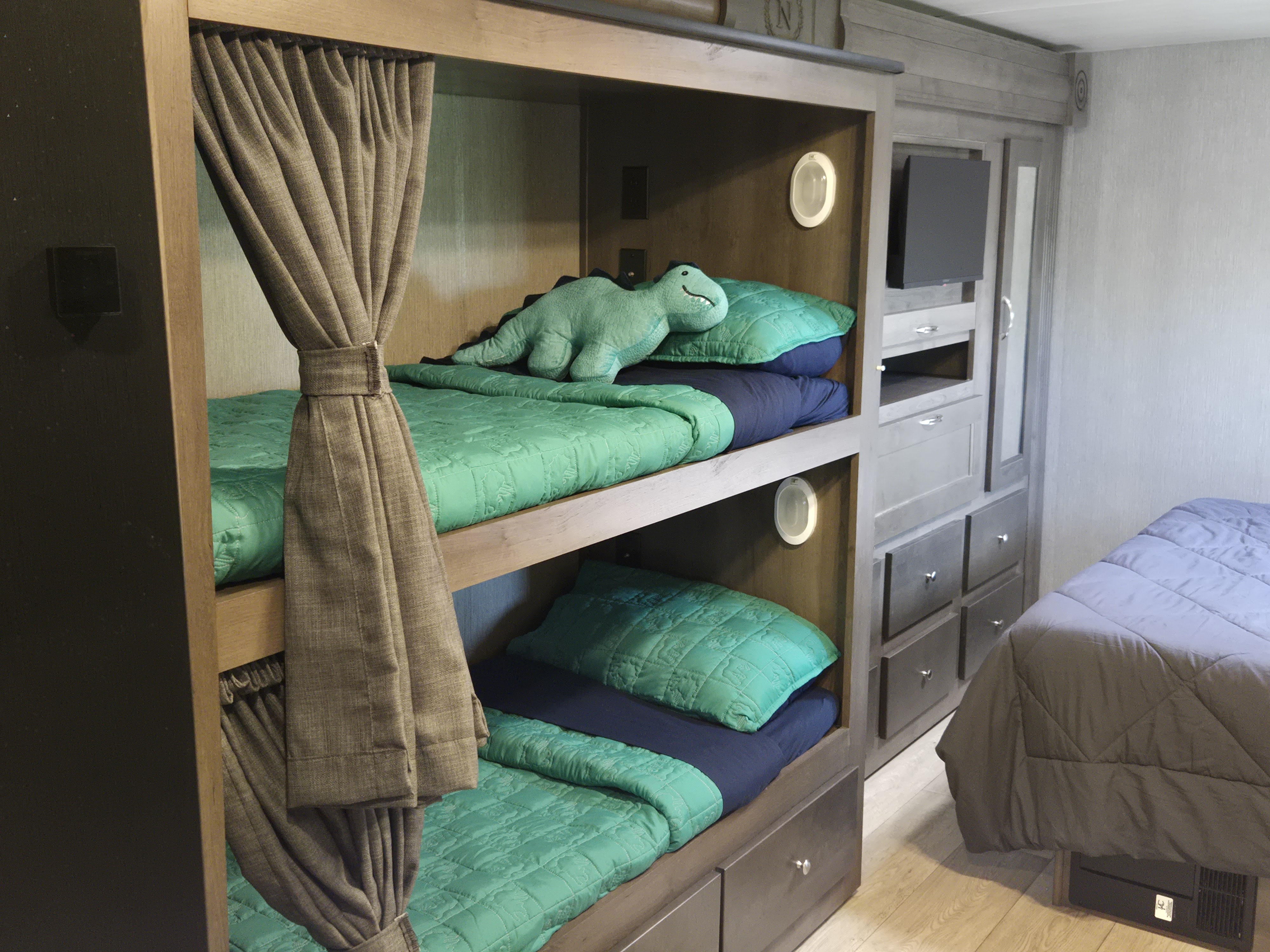 Cozy bunk beds & storage in an RV rental, featuring green bedding, a dinosaur toy, and built-in storage.. Nexus RV Phantom 2024