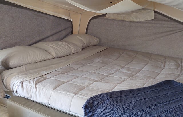 Experience comfort in your RV rental: a cozy bed with pillows, a quilted comforter, and a blue blanket inside a camper.. Forest River Rockwood Freedom 2021