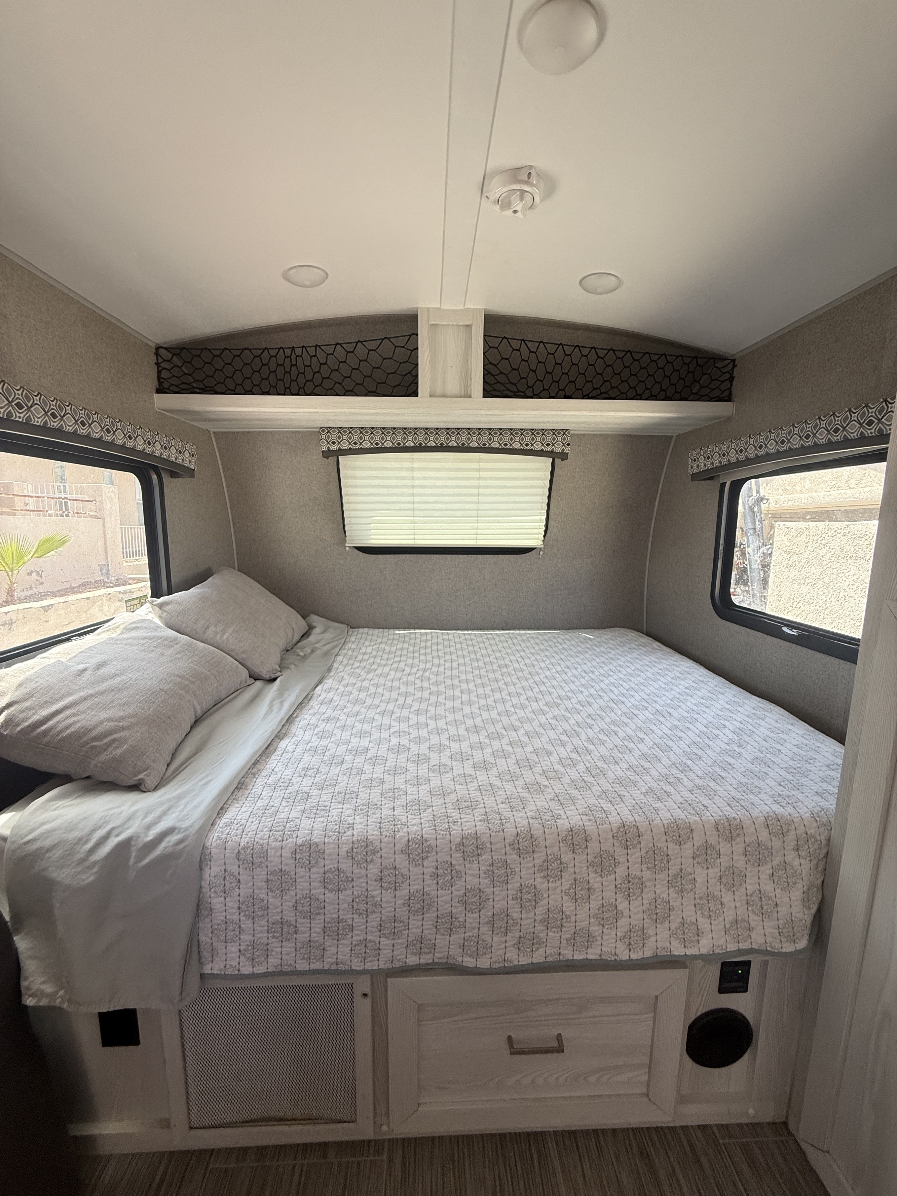 Cozy rv rental bedroom showing a large bed with pillows, patterned quilt, multiple windows, and overhead netted storage.. Forest River Flagstaff E-Pro 2018