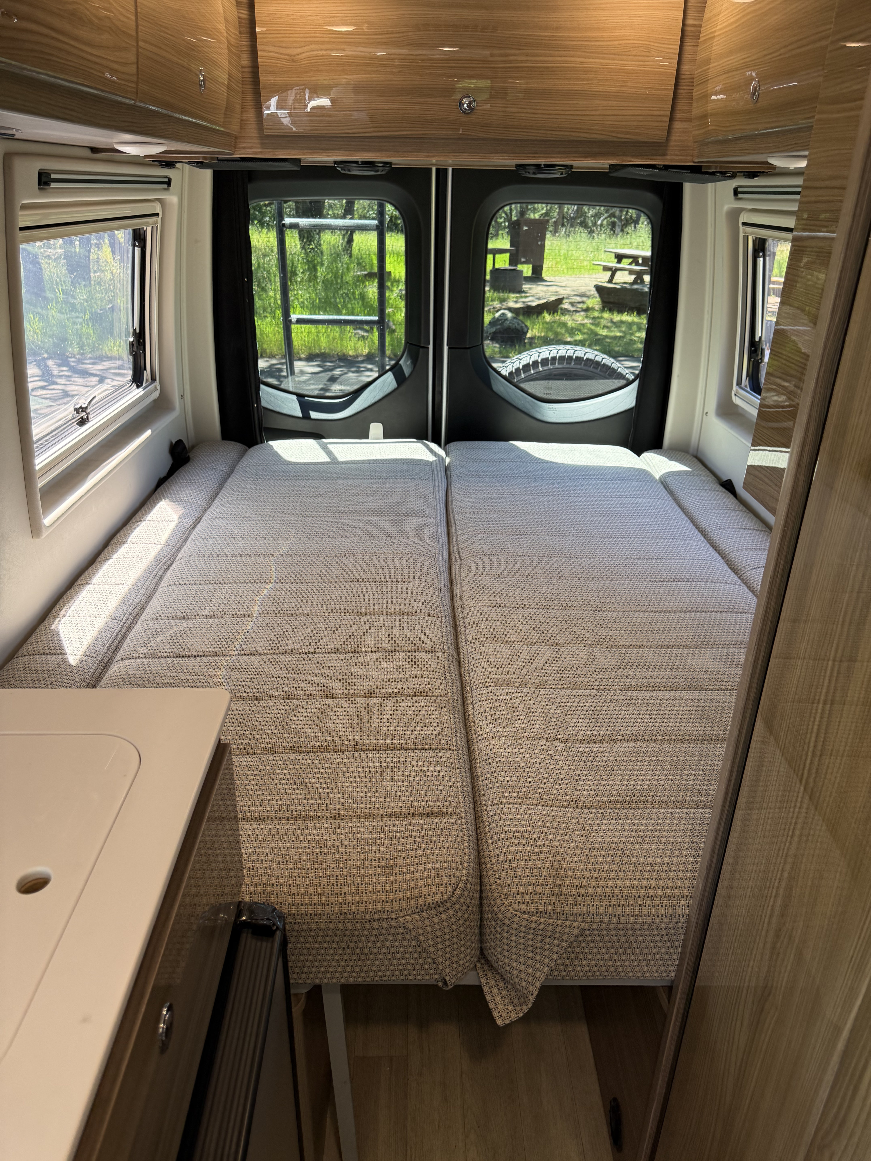 Comfortable side-by-side beds in this rv rental's spacious interior, offering scenic campsite views through large windows.. Winnebago Boldt 2020