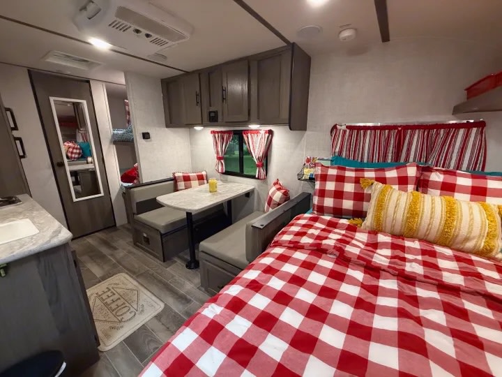 Cozy RV rental interior showcasing a red & white checkered bed, dinette, kitchen area, and bunk beds.. Gulf Stream Ameri-Lite Super Lite 2019