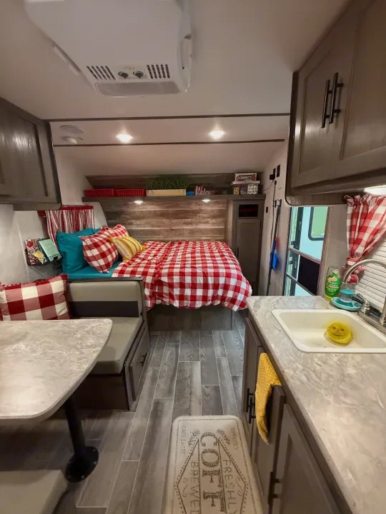 Cozy RV rental interior: bed with red gingham, dinette, and compact kitchen area. Features rustic wood accents & wood-look floors.. Gulf Stream Ameri-Lite Super Lite 2019