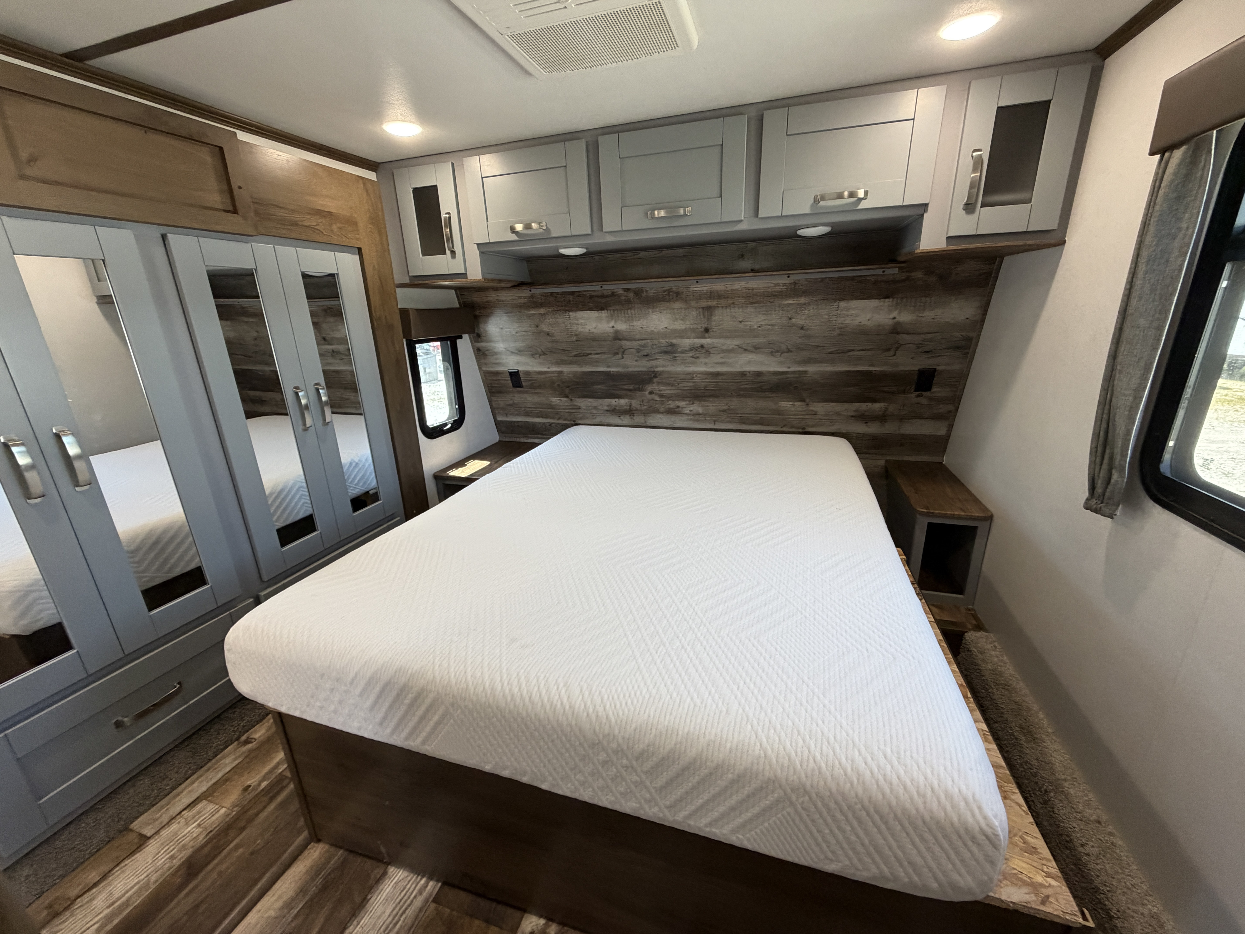 Inside an RV rental, a modern bedroom with a large bed, grey overhead cabinets, mirrored wardrobe, and wood paneling accents.. Keystone RV Fuzion Toy Hauler 2020