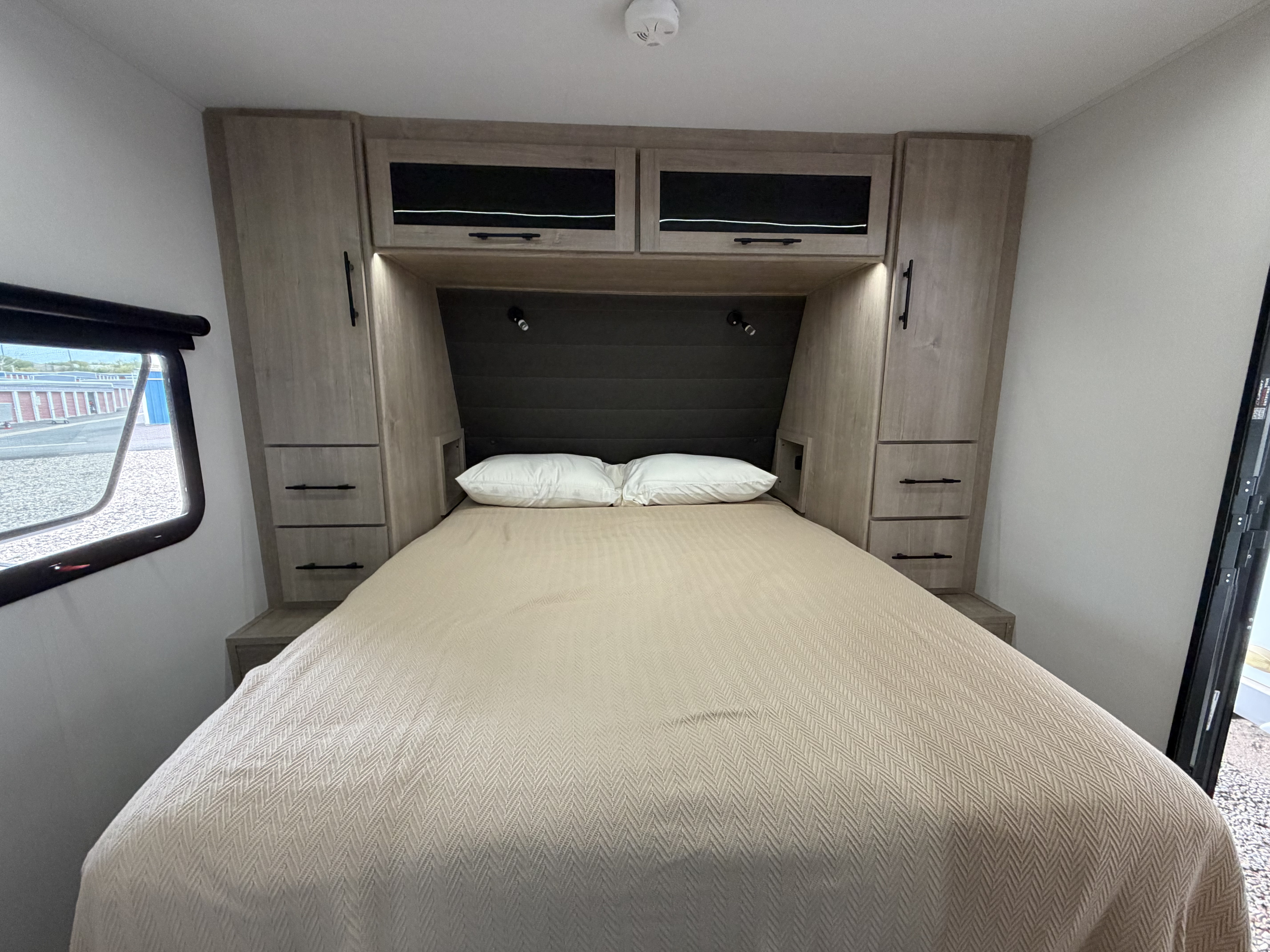Cozy RV rental bedroom featuring a queen bed, built-in storage, and reading lights, ideal for your next travel trailer trip.. Grand Design Imagine XLS 2025