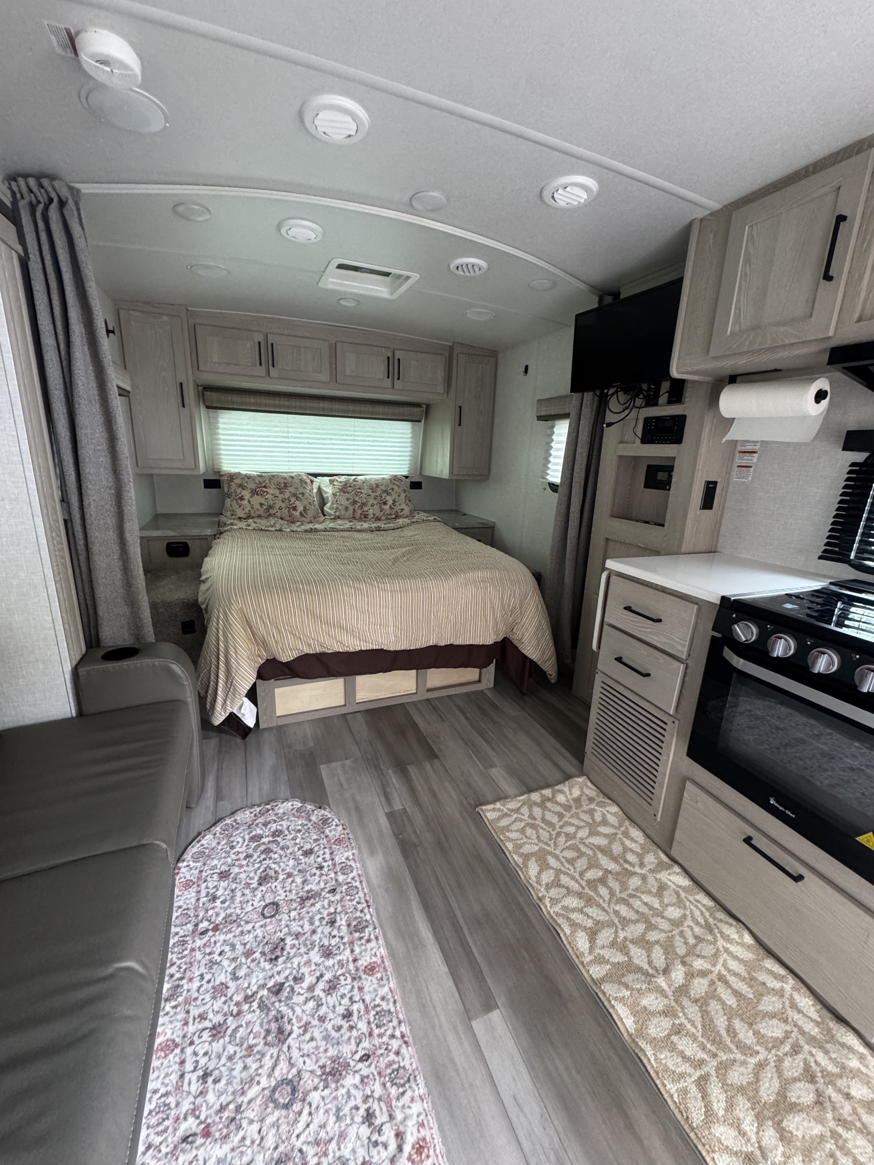 Modern RV rental interior of a travel trailer, featuring a bed, kitchen with stove, and sofa. Cozy and well-equipped.. Forest River Flagstaff Micro Lite 2021