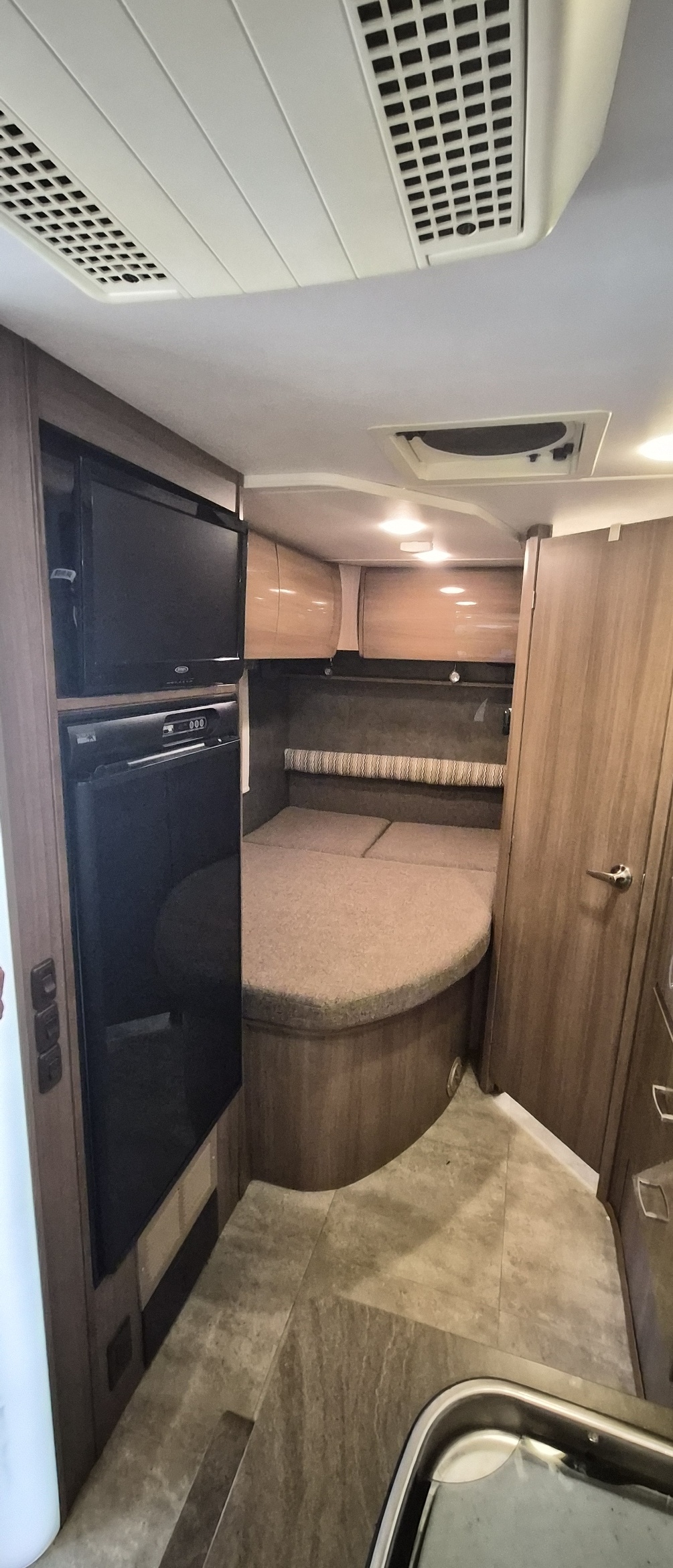 Step into this cozy rv rental interior. Features a comfortable bed, TV, fridge, sink, and overhead cabinets for compact travel.. Winnebago Trend 2015