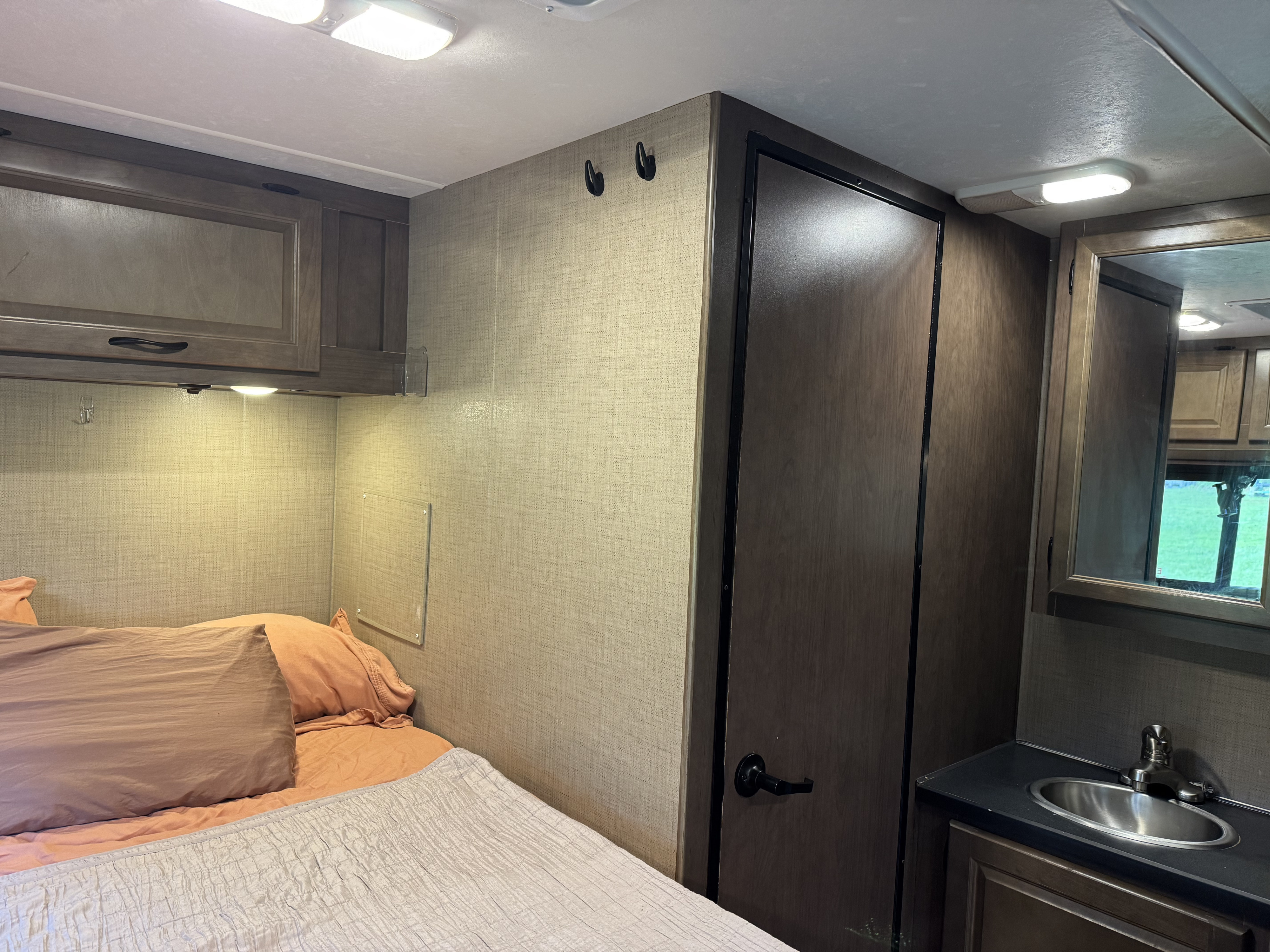 This rv rental offers a sleeping area with a bed, storage cabinets, and a compact bathroom vanity with a sink and mirror.. Thor Majestic 2018