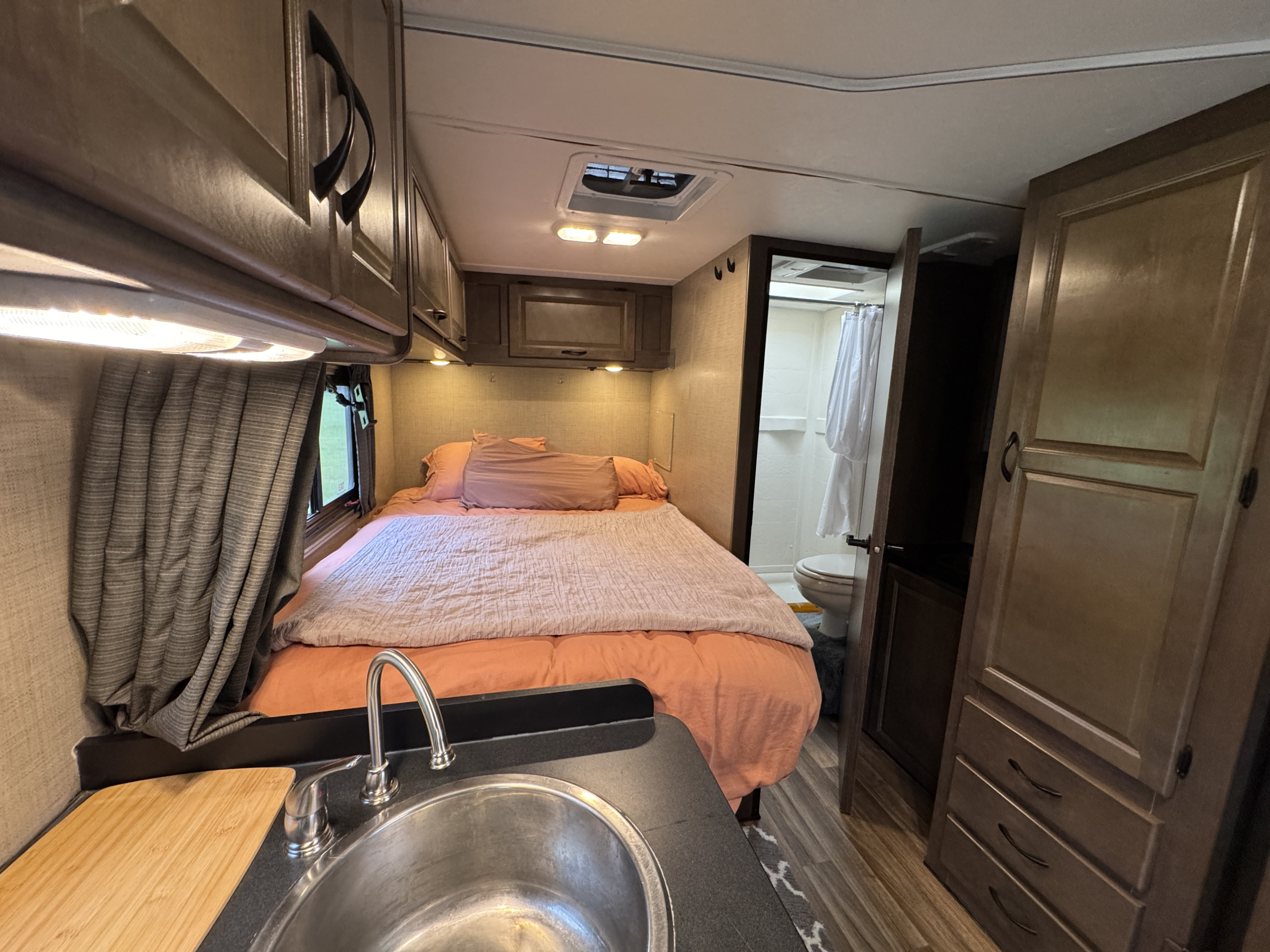 Cozy RV rental interior featuring a bed, sink, and bathroom. Overhead cabinets and window provide comfort and functionality.. Thor Majestic 2018