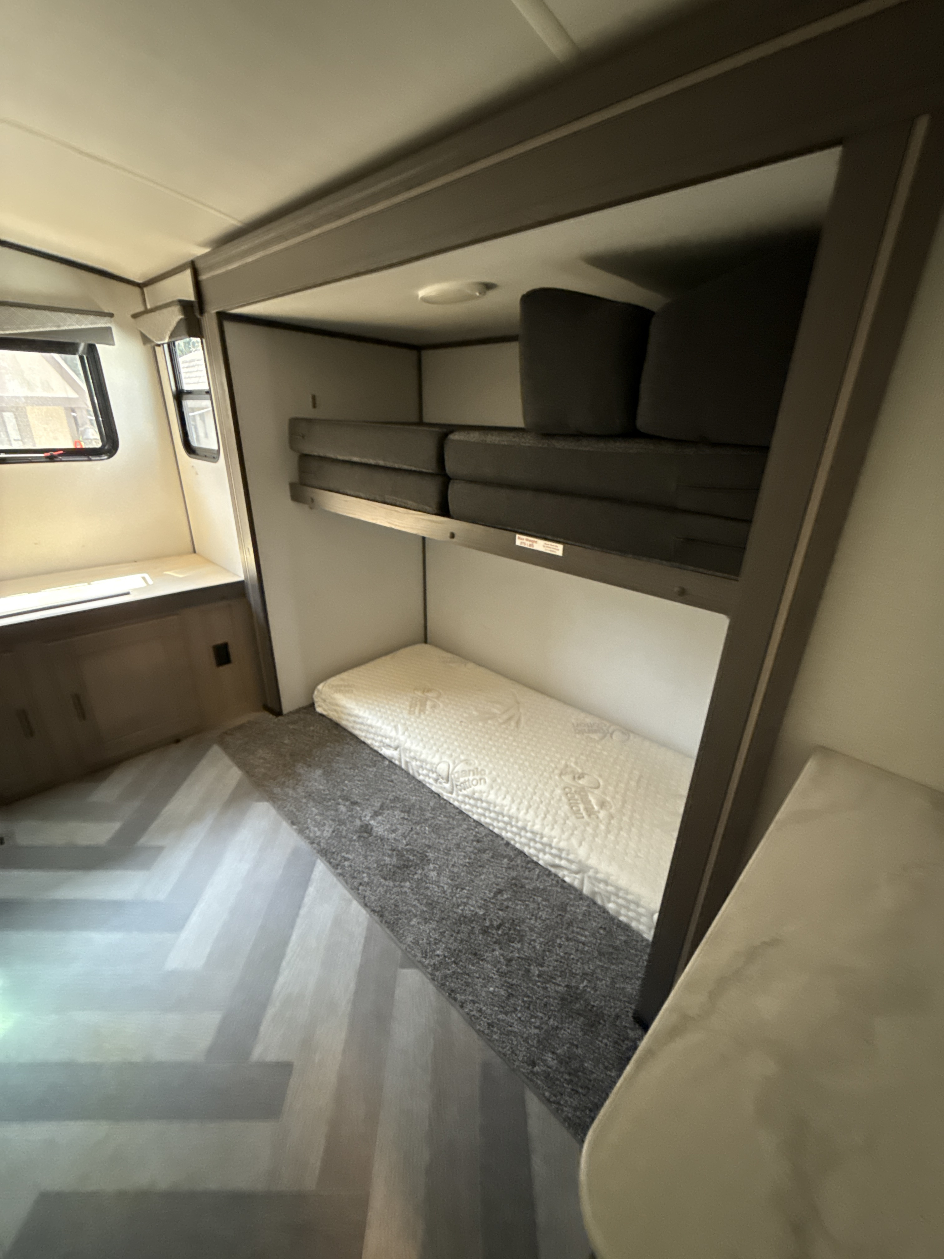 An RV rental's bunk bed area. Upper bunk has dark cushions, lower has a white mattress. Features stylish herringbone flooring.. Twilight RVS Signature 2021