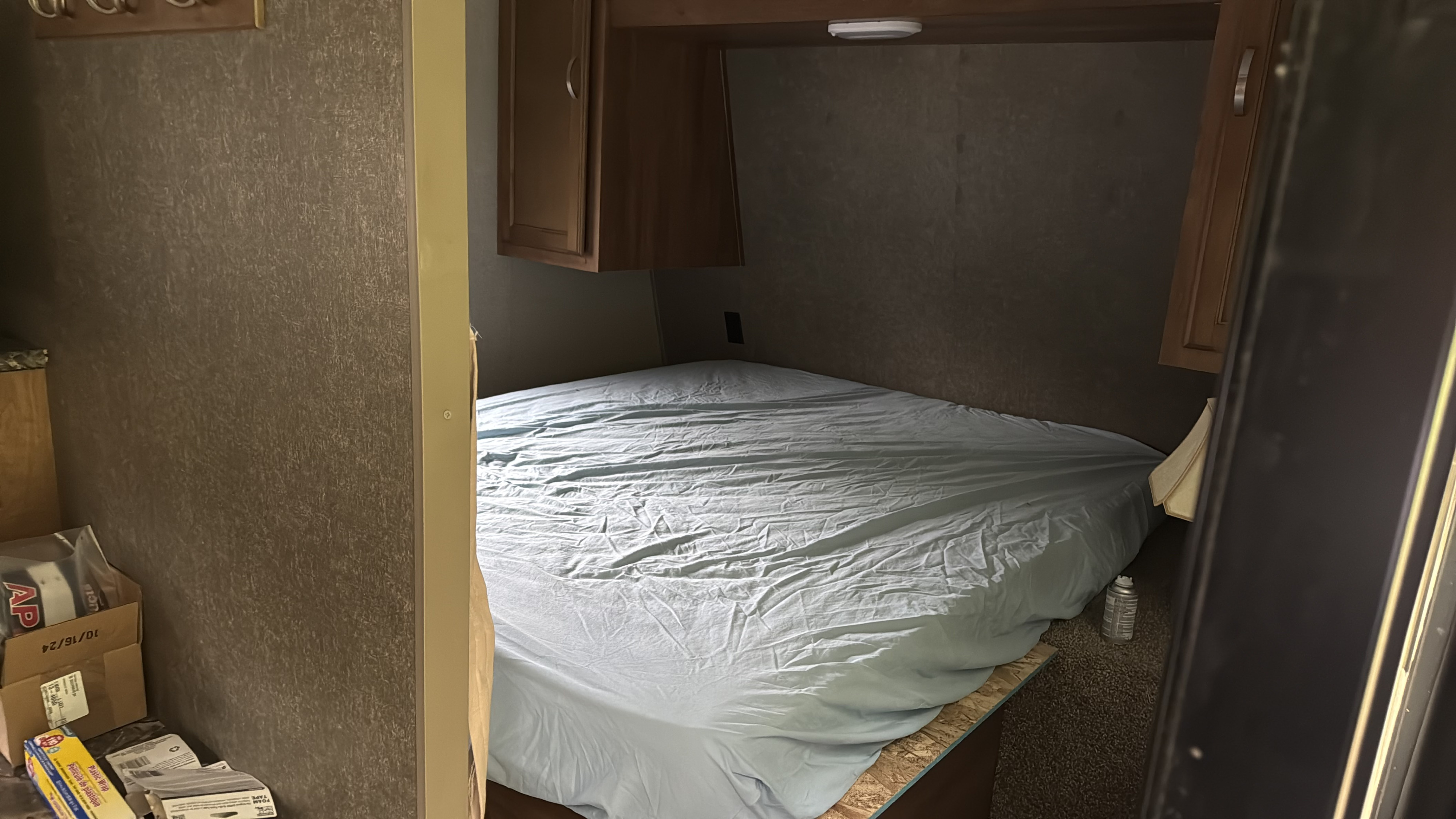 RV rental bedroom featuring a tucked-in bed with light blue sheets and practical overhead cabinets. Trailer interior view.. Keystone RV Springdale 2018