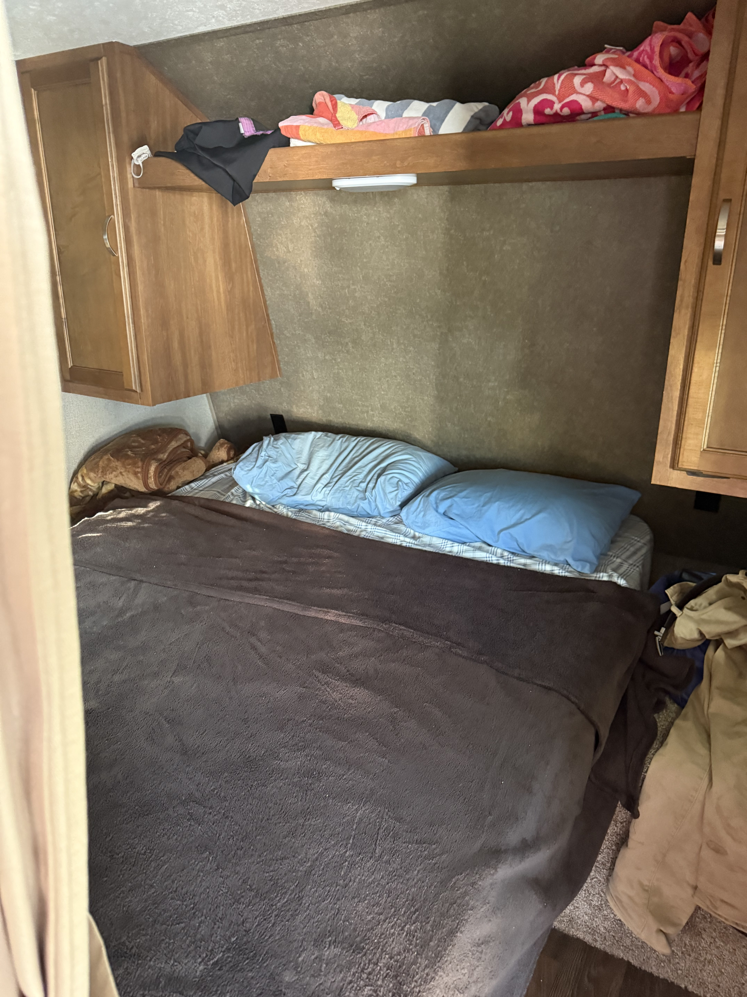 Inside an RV rental: a snug bedroom with bed, light blue pillows, blankets, and storage above, perfect for travel.. Keystone RV Springdale 2018