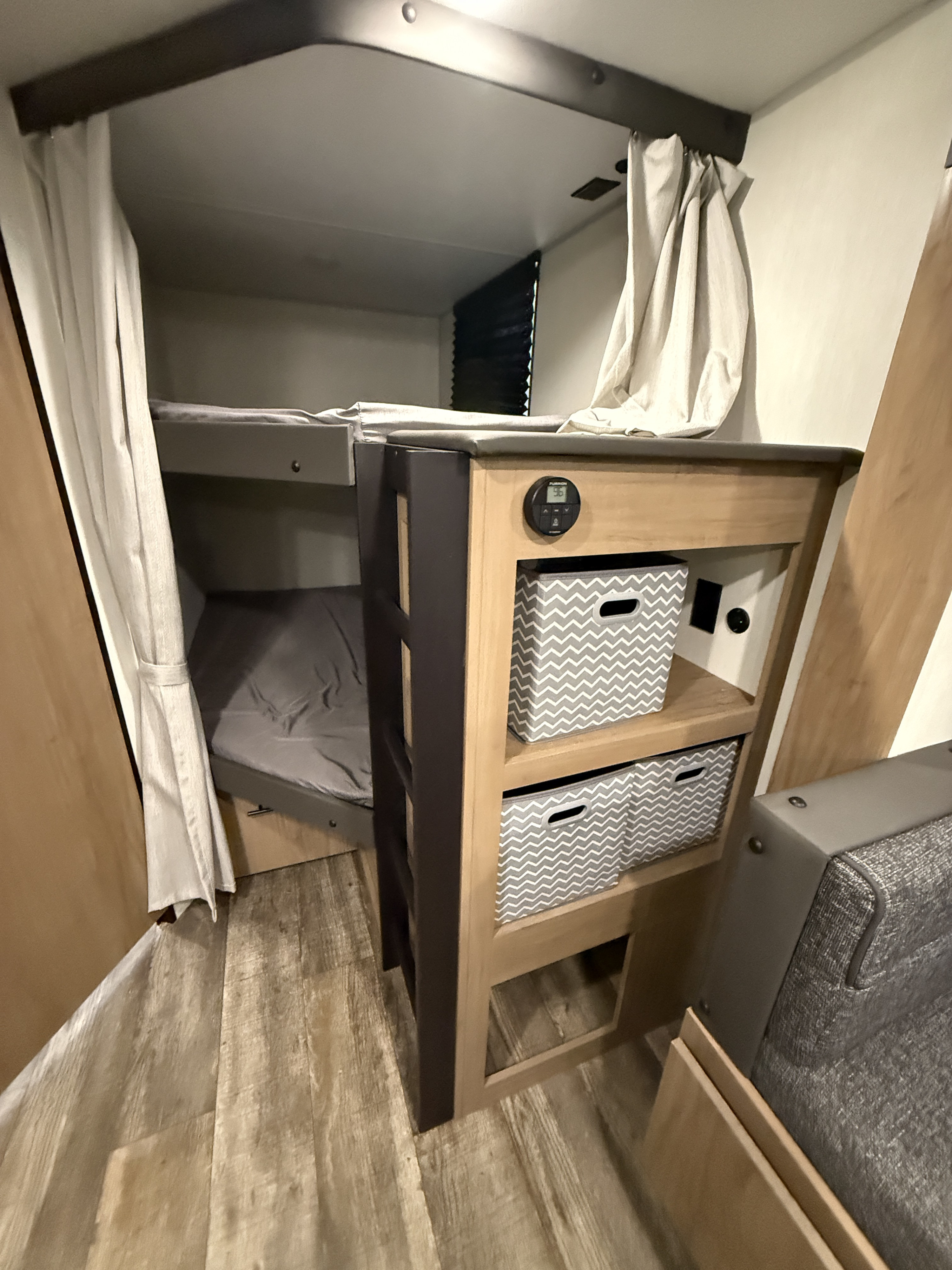 Inside an RV rental: built-in bunk beds with privacy curtains, and a storage unit featuring bins and a digital control panel.. Forest River Campsite Reserve 2025