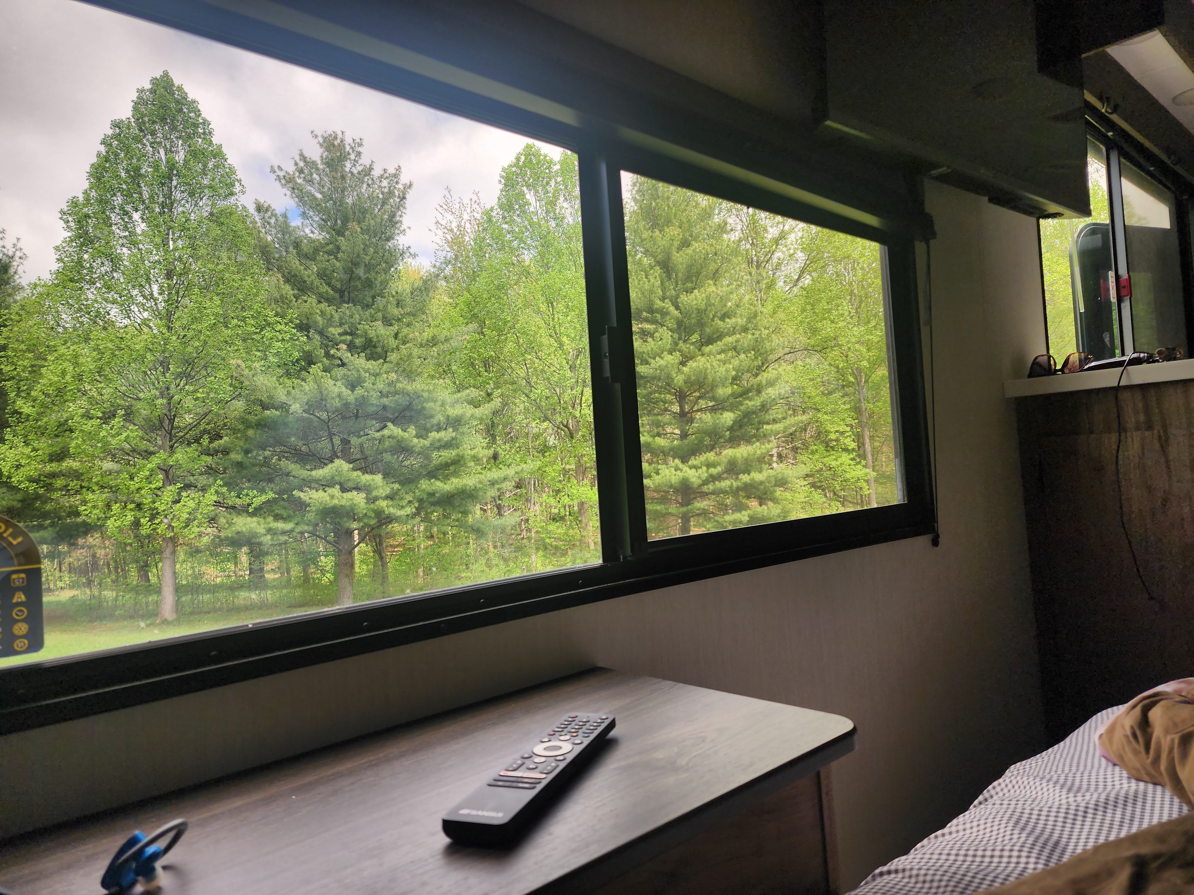 Cozy RV rental interior with a window view of a lush green forest. Remote on the table, offering a peaceful escape.. Forest River 19KB 2025