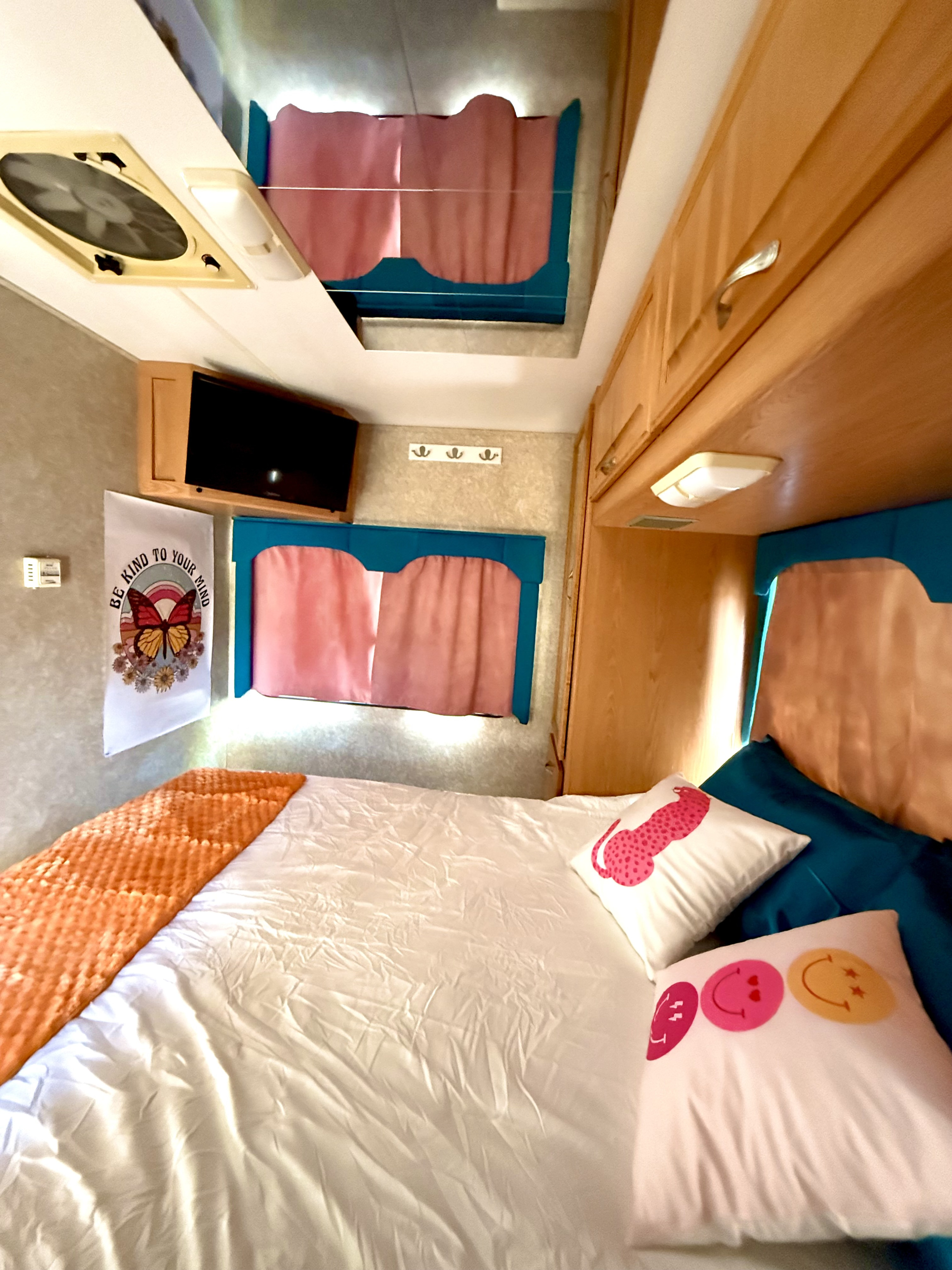 Inviting RV rental interior featuring a bed with vibrant pillows, a TV, and charming butterfly wall art in a cozy bedroom setup.. Four Winds 5000 2005