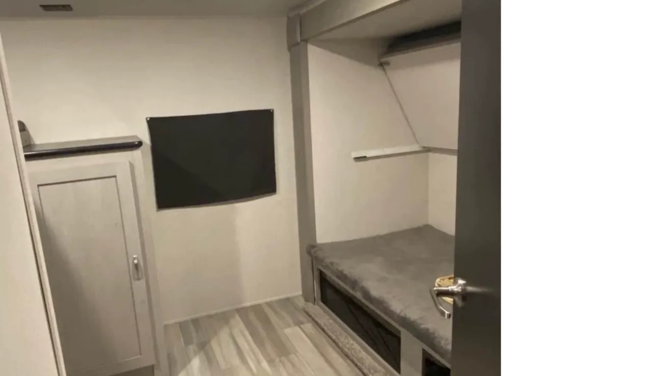 RV rental bunk room with a gray bed, overhead shelf, wall-mounted TV, and cabinet for compact travel living.. Forest River Tracer 2022