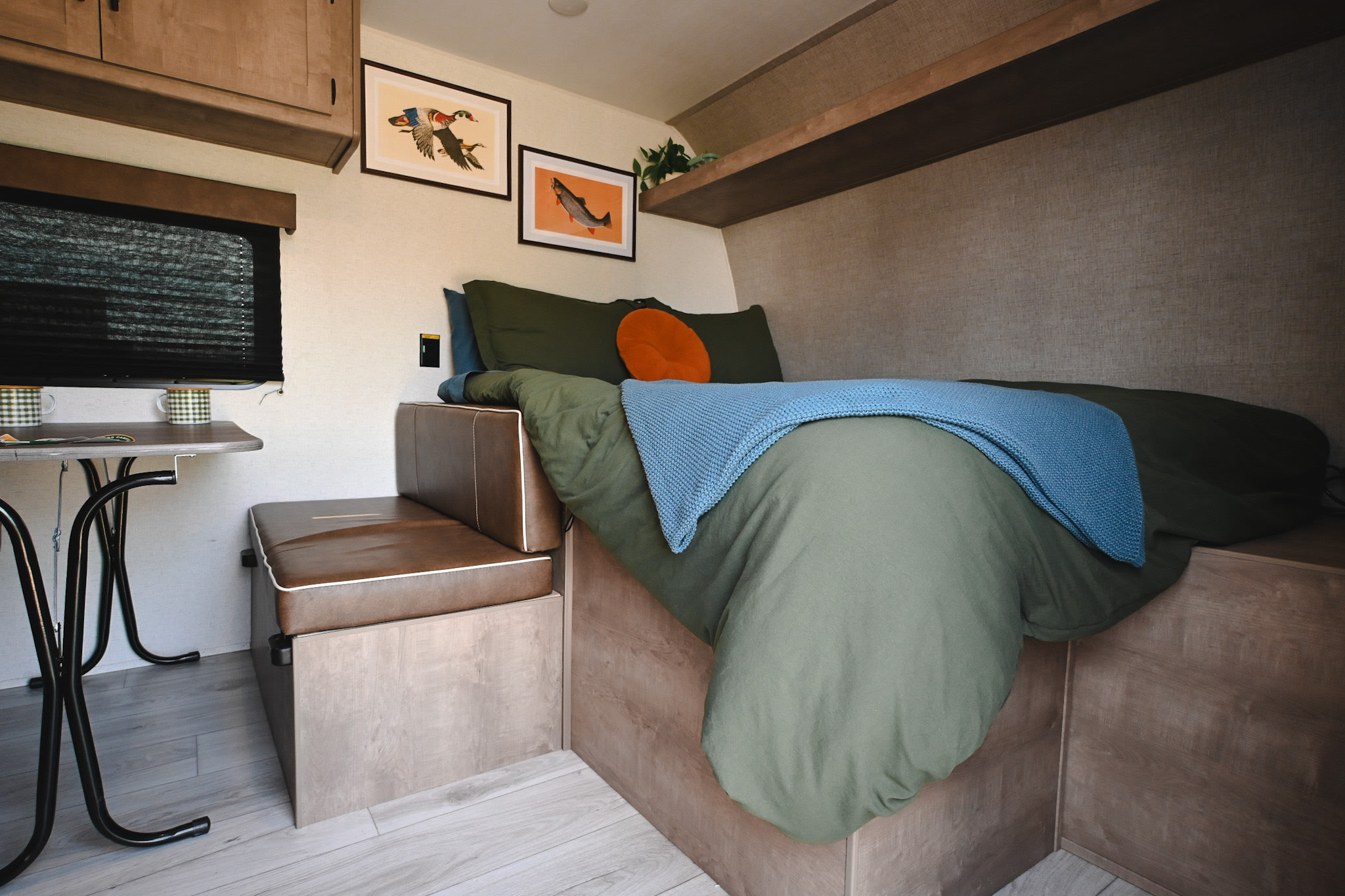 Relax in this cozy rv rental bedroom featuring a green bed, blue throw, nature art, and practical dinette.. Keystone RV Springdale Mini 2025