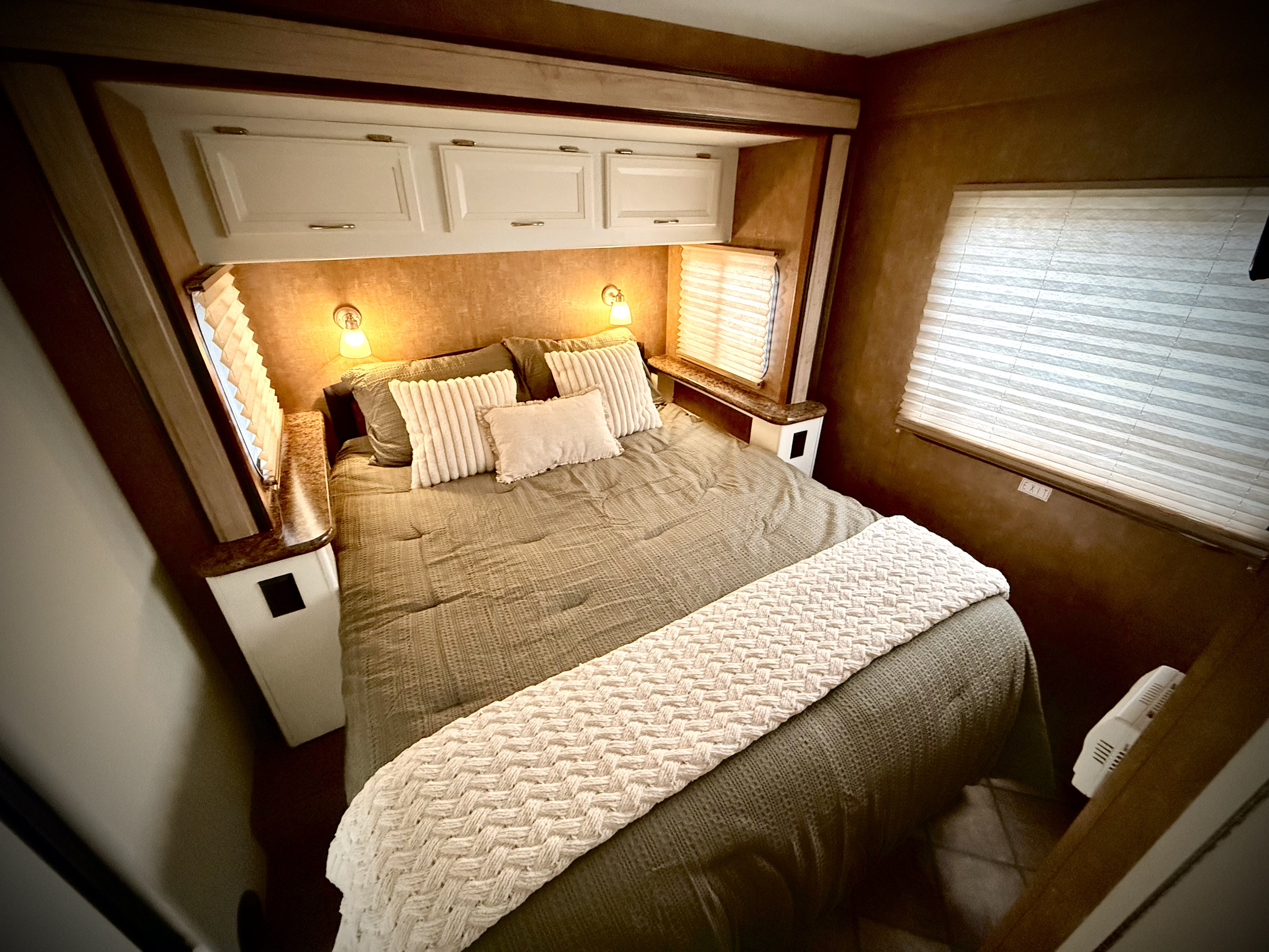 Cozy RV rental bedroom with warm lighting, green bedding, and overhead cabinets. Perfect for comfortable travel.. Thor Four Winds 2014