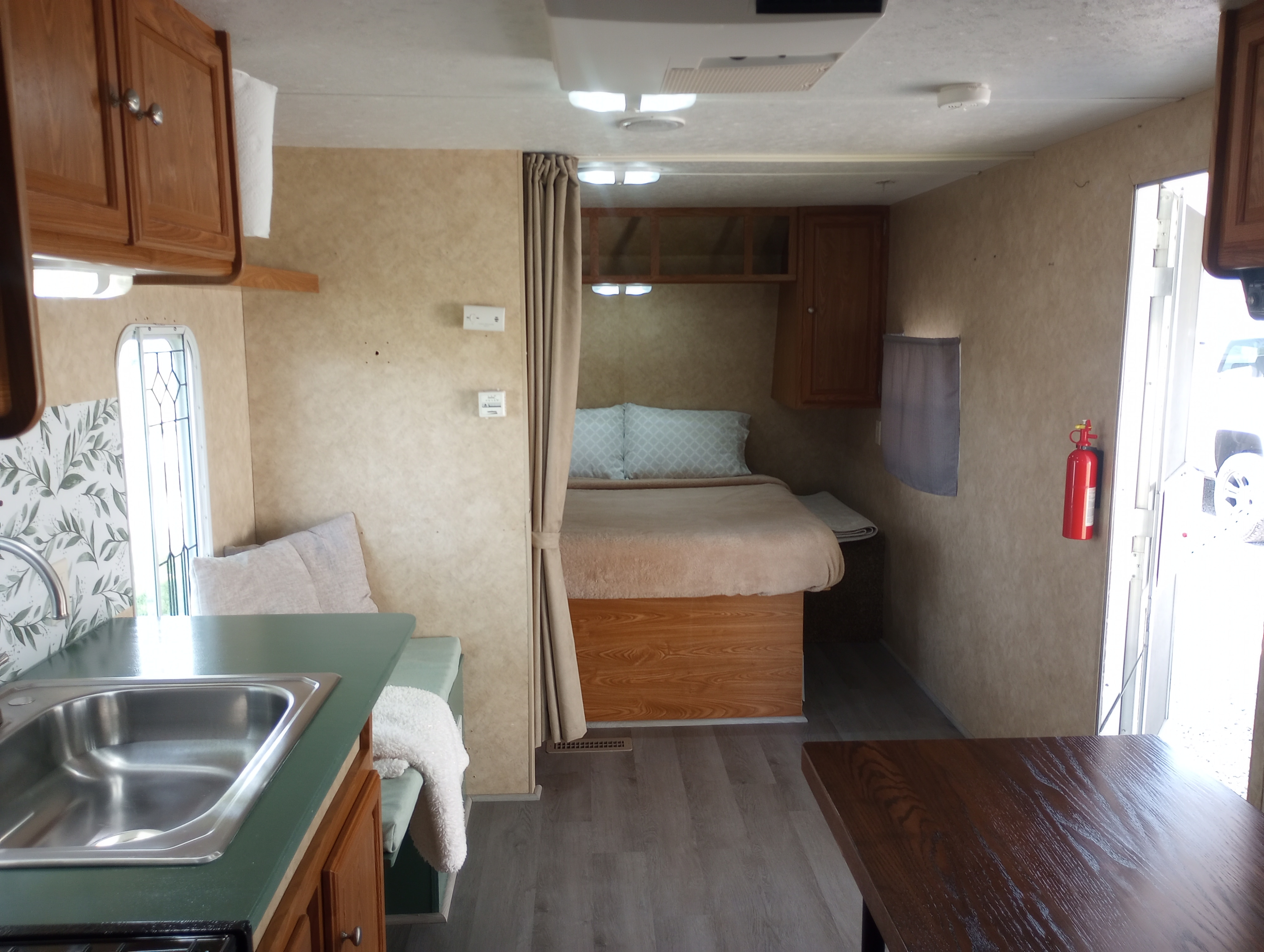 Spacious RV rental interior with kitchenette, dining booth, and private bedroom. Features a sink, bed, and privacy curtain for travel comfort.. Dutchmen Dutchmen Trailer 2008