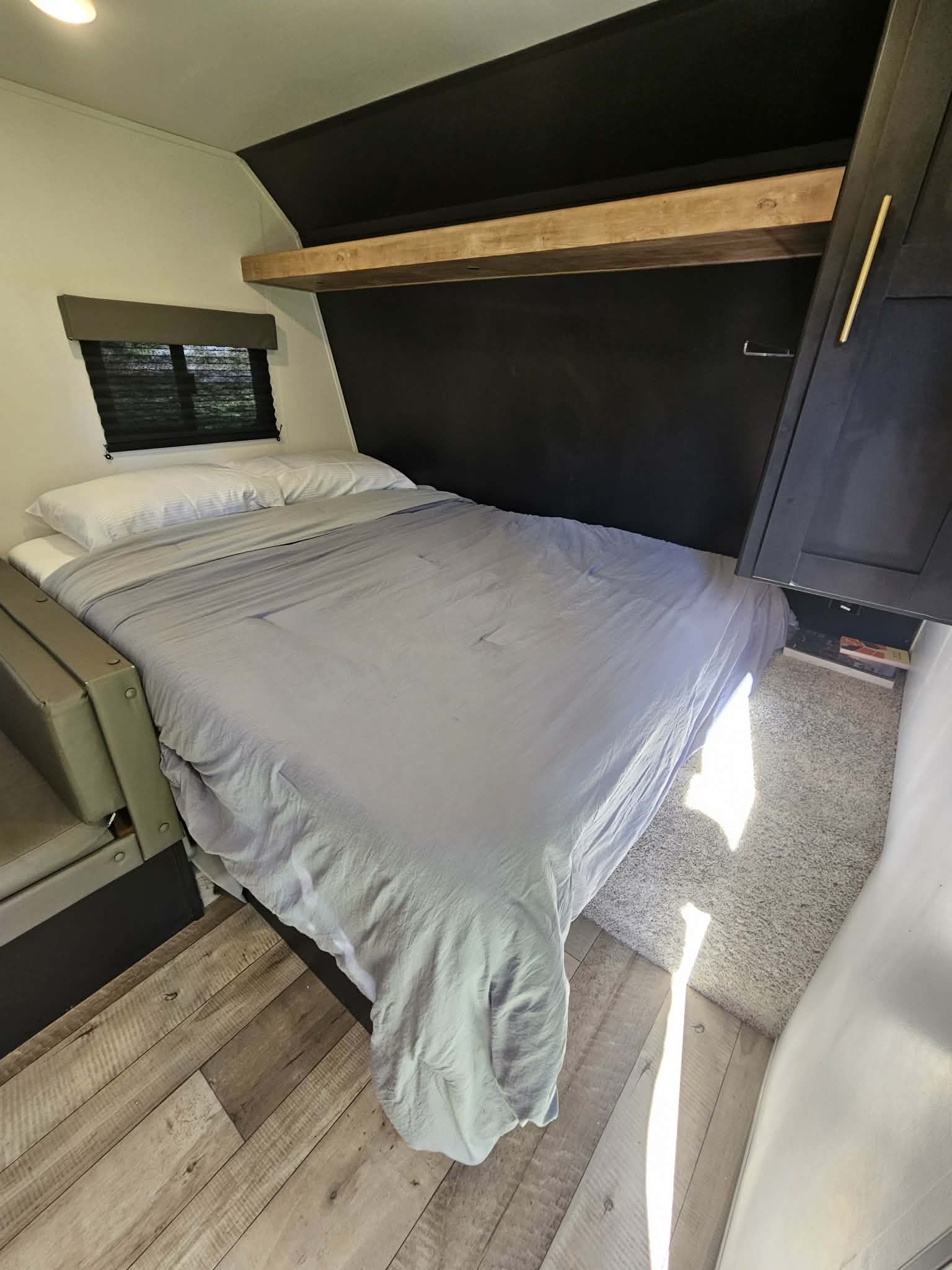 RV rental bedroom: a cozy bed with white pillows, wooden shelf, dark cabinet, and mixed flooring under sunlight.. Keystone RV Springdale 2022
