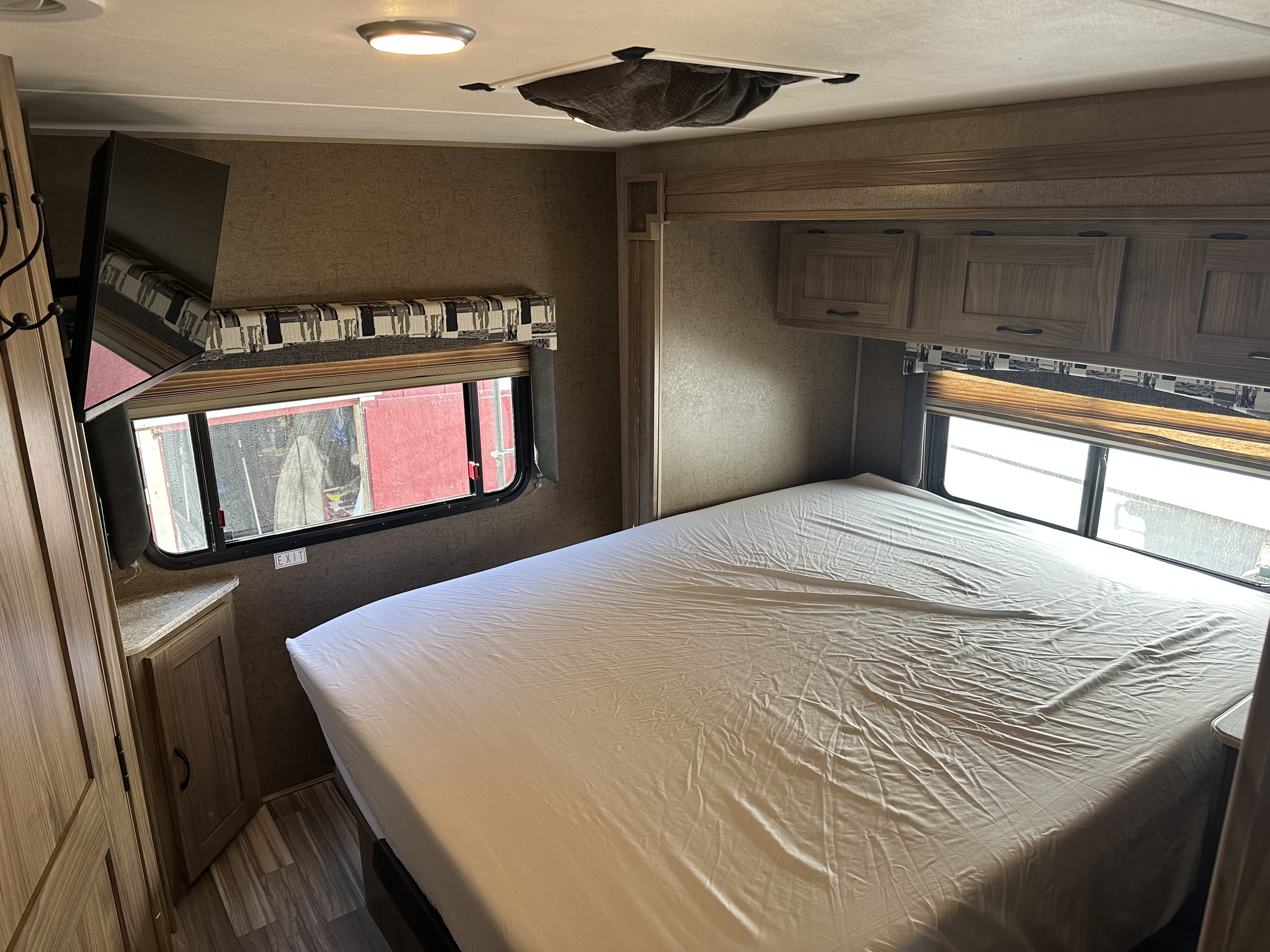 RV rental bedroom with bed, wall-mounted TV, windows, and overhead cabinets for a comfortable stay.. Coachmen Freelander 2015