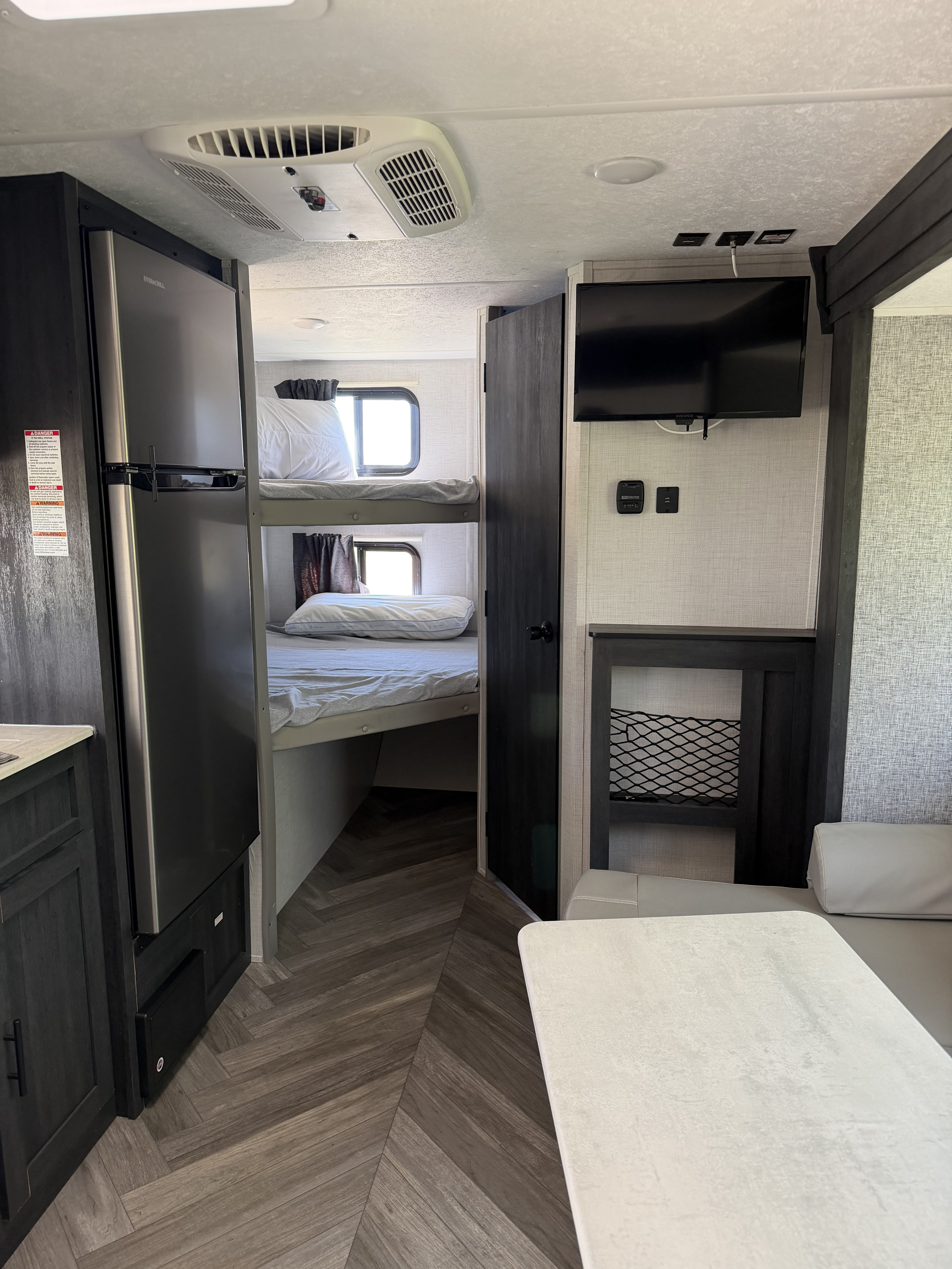 Inside a modern rv rental: bunk beds, fridge, dining area, TV, and AC unit. Neutral decor, herringbone flooring.. Forest River RV Ozark 2021