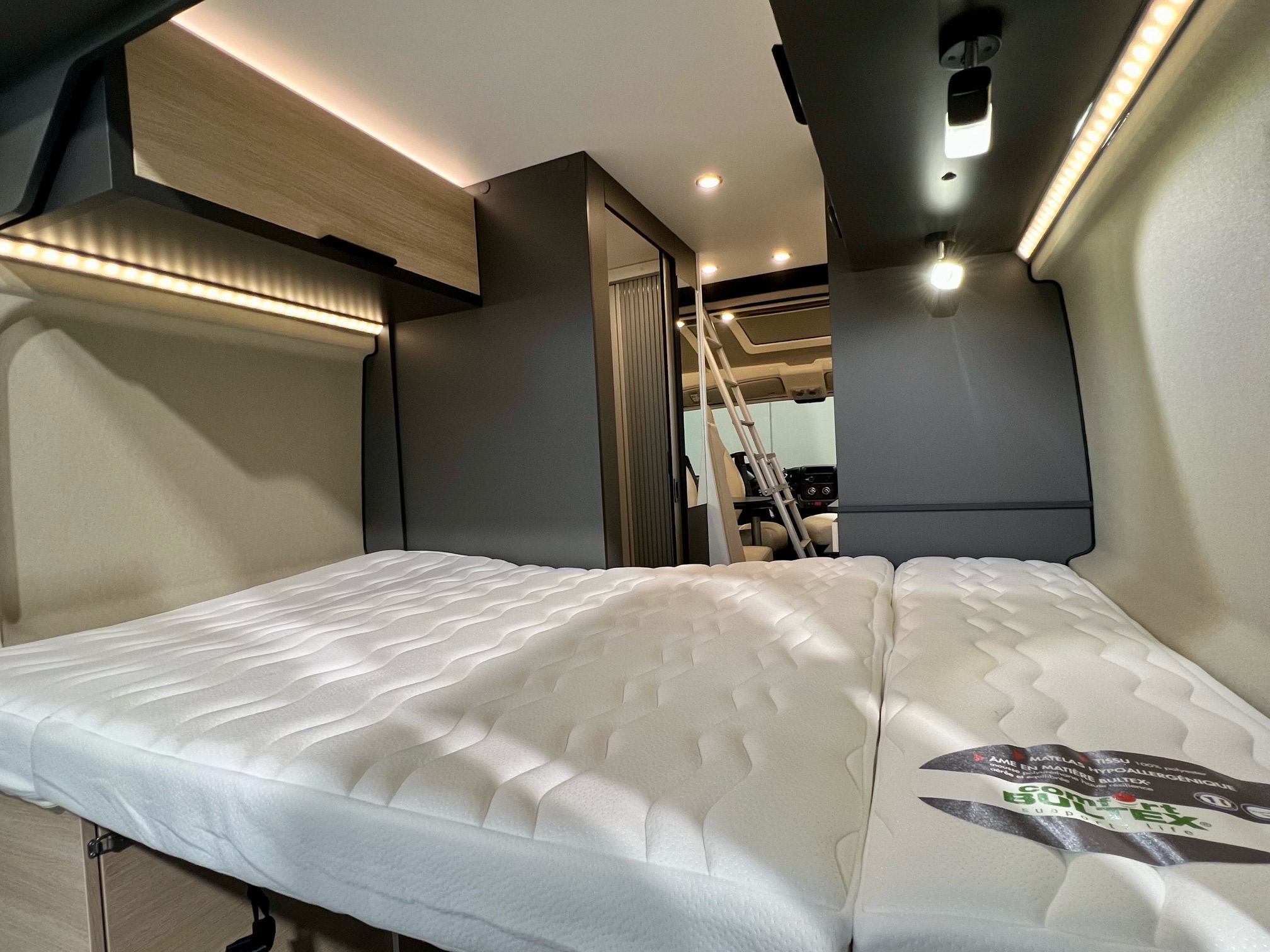 RV rental interior: cozy bedroom area with two plush mattresses, overhead storage, and ambient LED strip lighting for a comfortable stay.. DREAMER D43 2026