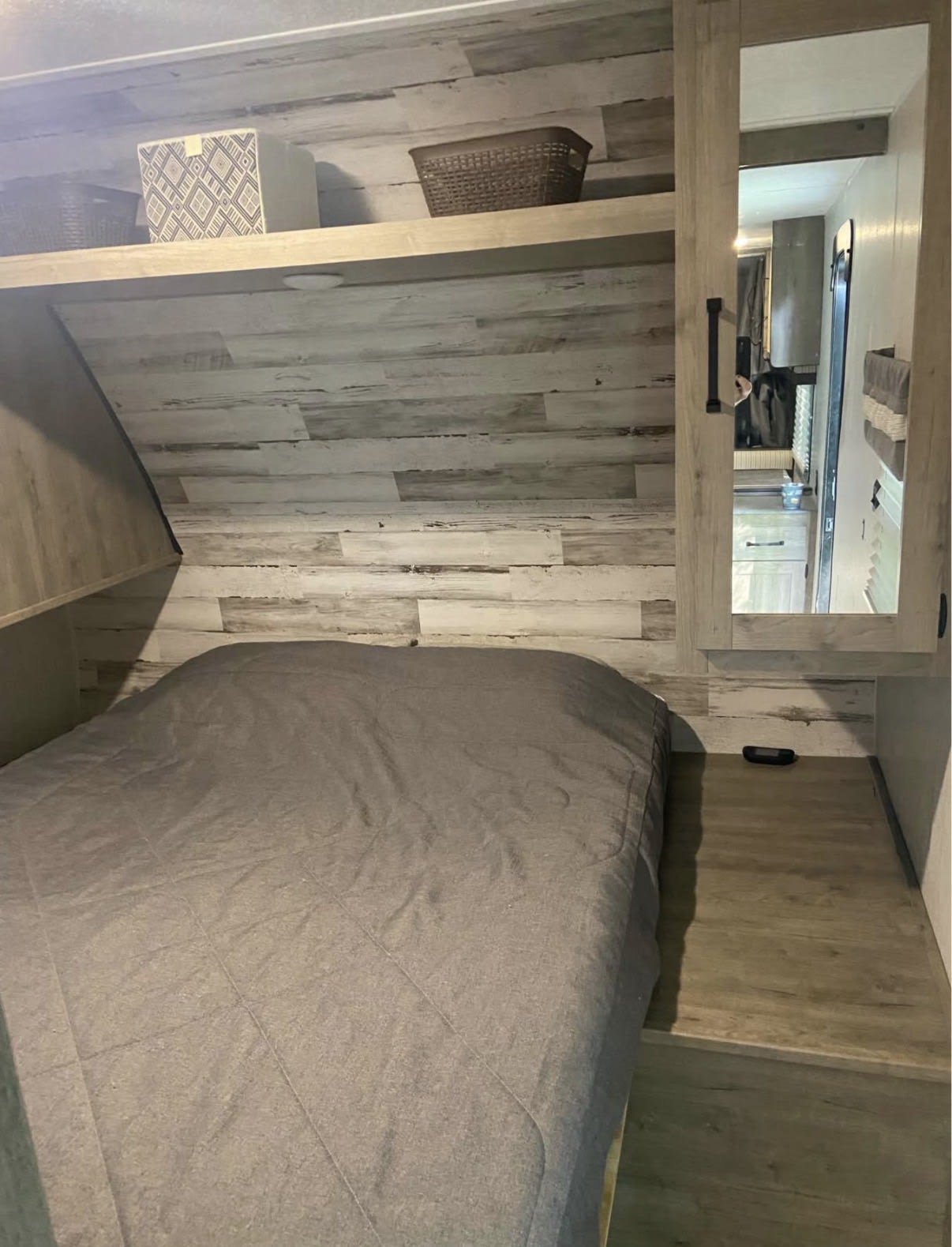 Compact RV rental bedroom featuring a gray-covered bed, wood-look paneling, overhead shelf, and mirrored cabinet.. Palomino Puma 2021