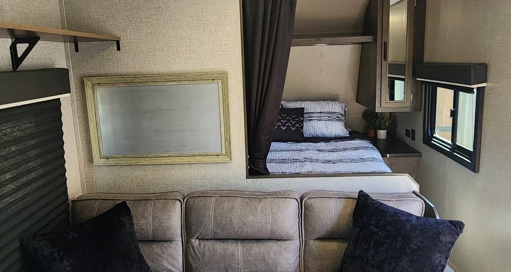 Cozy rv rental living space with a sofa, a private bed behind a curtain, a wall mirror, and windows. Ideal for travel comfort.. Jayco Jay Flight SLX Rocky Mountain Edition 2020