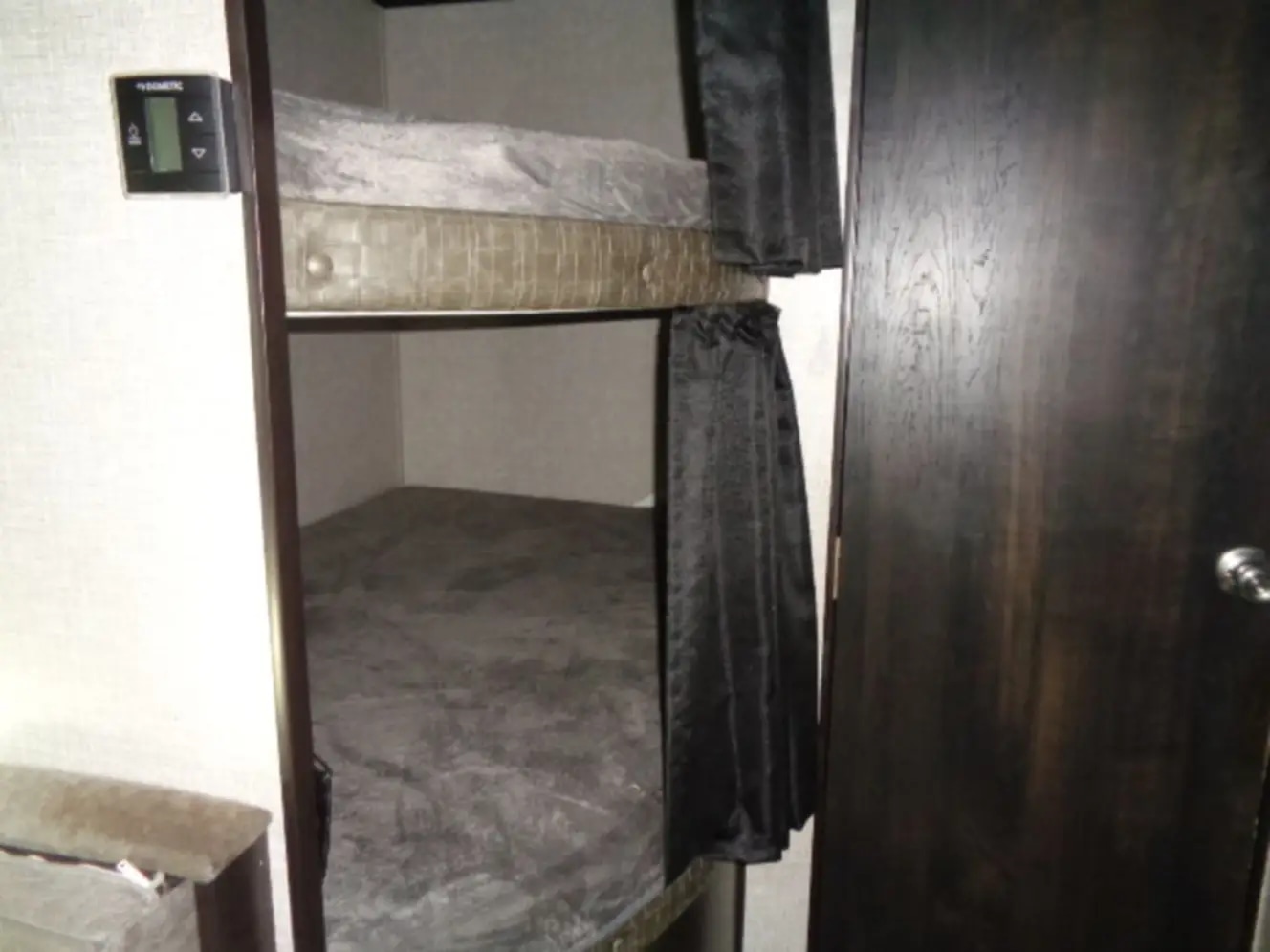 RV rental bunk beds: a cozy sleeping area with dark privacy curtains and a Dometic thermostat visible on the wall.. Jayco Jay Flight 2022