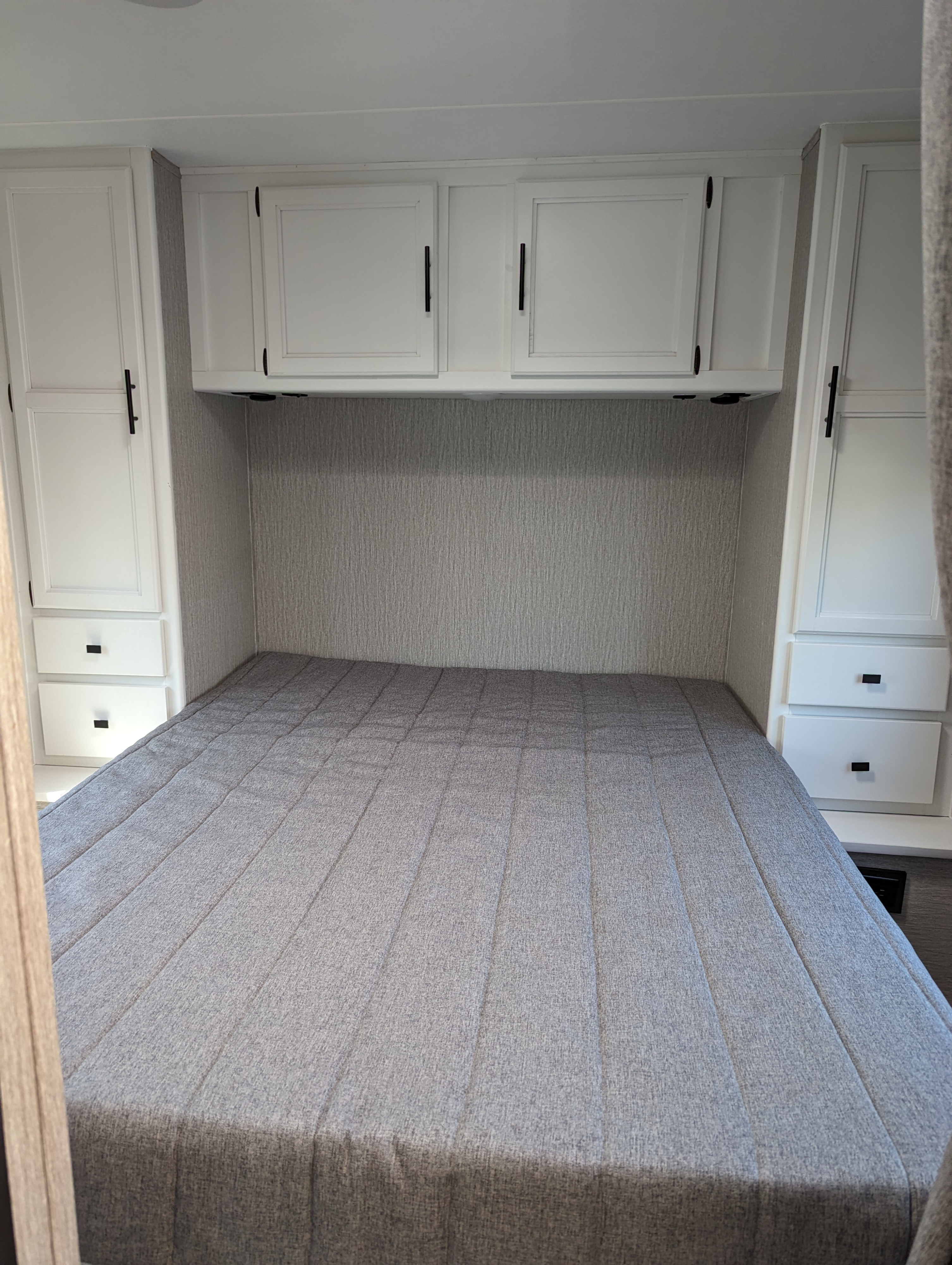 This RV rental bedroom offers a gray bed, white overhead and side cabinets, maximizing storage in a clean, compact design.. Coachmen Cross Trail XL 2022