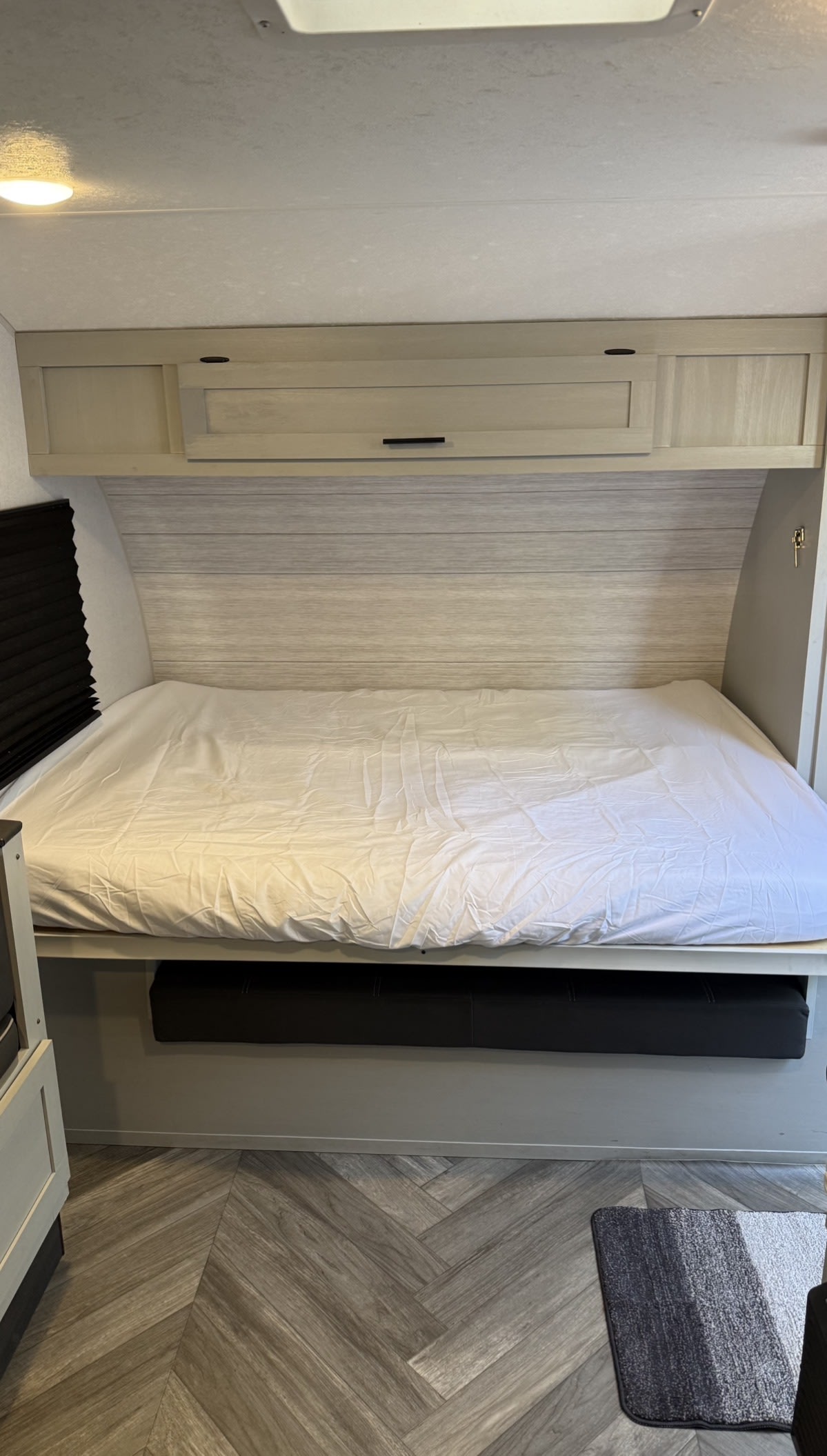 RV rental bed with white sheets, light wood cabinets above, and herringbone flooring. Compact and ready for travelers.. Forest River Salem FSX 2022