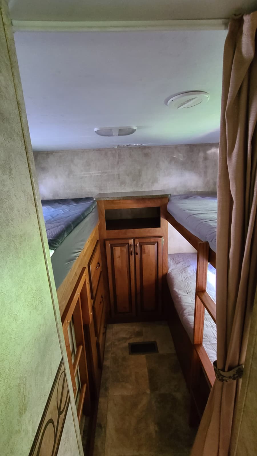 RV rental bunk room showing four beds, central wooden storage, and tiled floor.. Keystone RV Laredo 2011