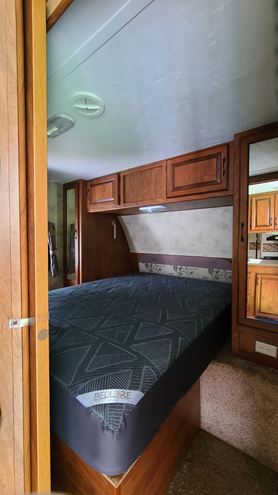 Cozy RV rental bedroom with a bed, wood cabinets, overhead storage, and ceiling fixtures. Your perfect home on wheels!. Keystone RV Laredo 2011